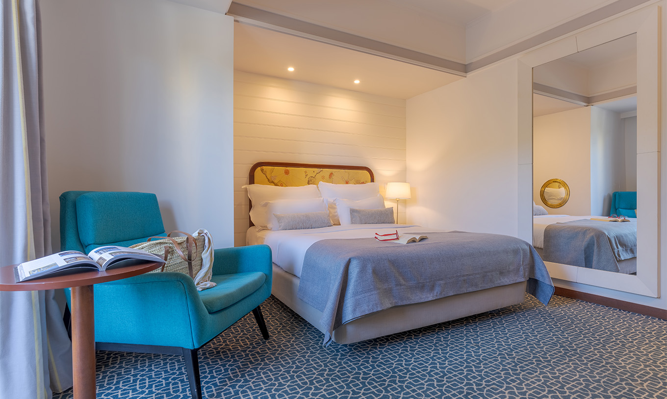 Le Deluxe du Pestana Alvor Praia a un lit double, une table avec fauteuil bleu, miroir et tapis avec motif