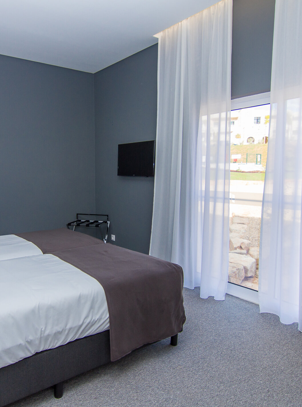 La chambre Classique du Pestana Gramacho Residences a deux lits simples, une télévision et une fenêtre avec rideaux