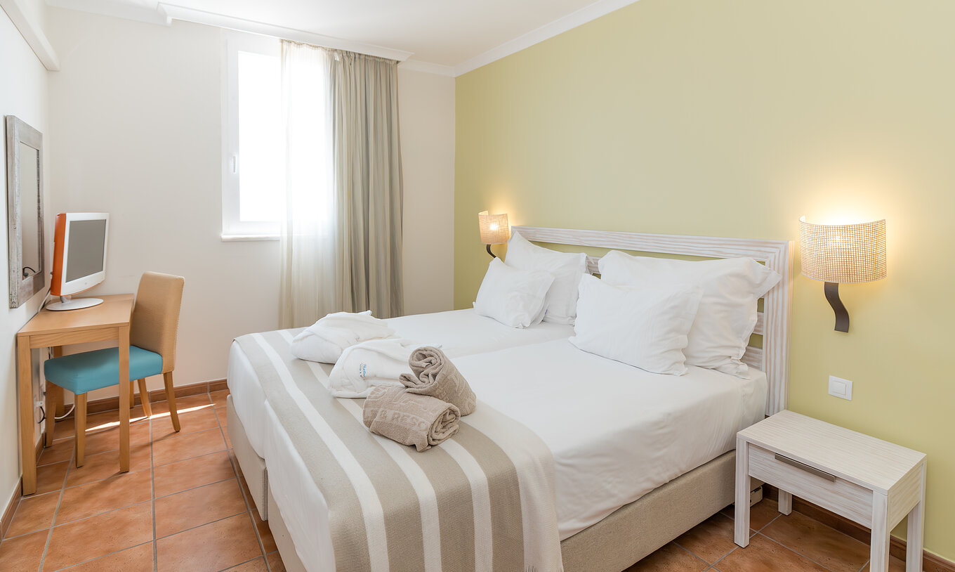 La Suite Vue Mer du Pestana Viking a une chambre avec deux lits, table de chevet et bureau avec chaise