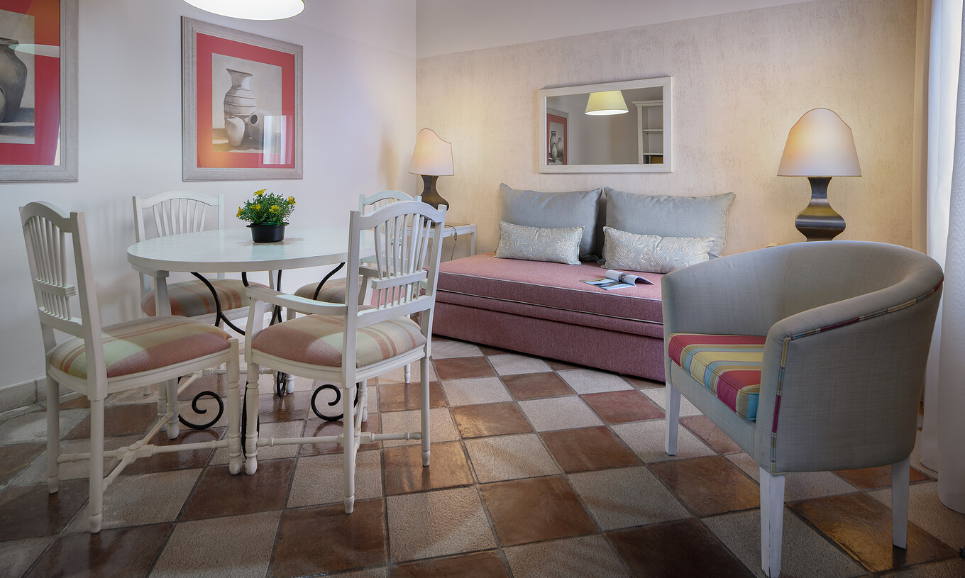 La Suite Vue Jardín du Pestana Vila Sol - Vilamoura a un salon avec un canapé, une table, des chaises et un miroir