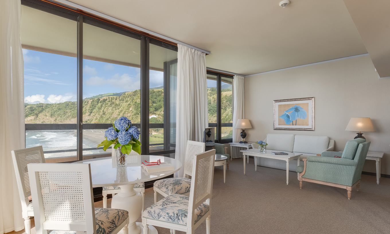 La Suite du Pestana Bahia Praia a un salon avec vue sur la plage à côté de l'hôtel et sur le paysage verdoyant