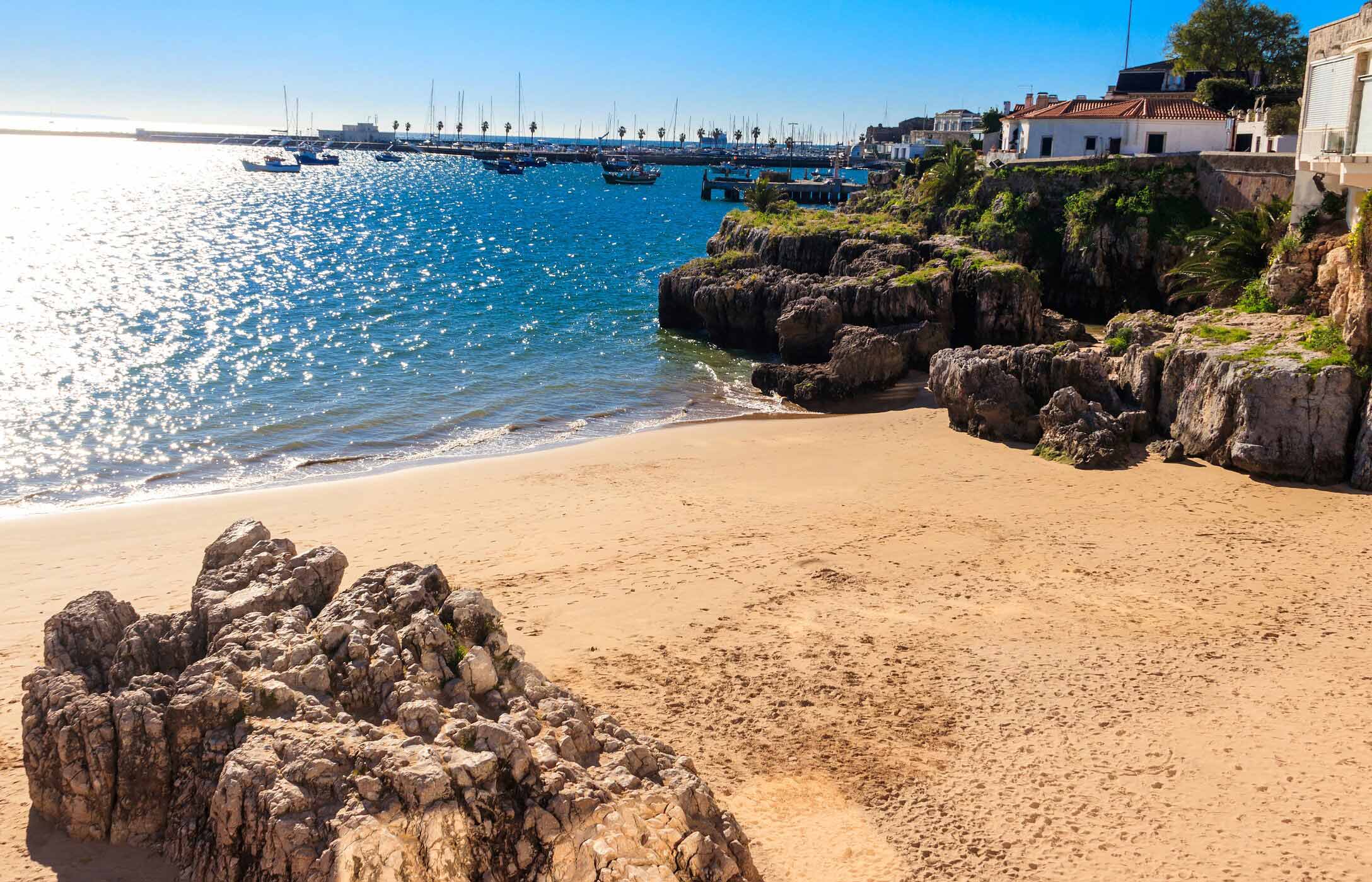 Petite plage à Cascais avec quelques rochers et de petits bateaux en arrière-plan dans la marina