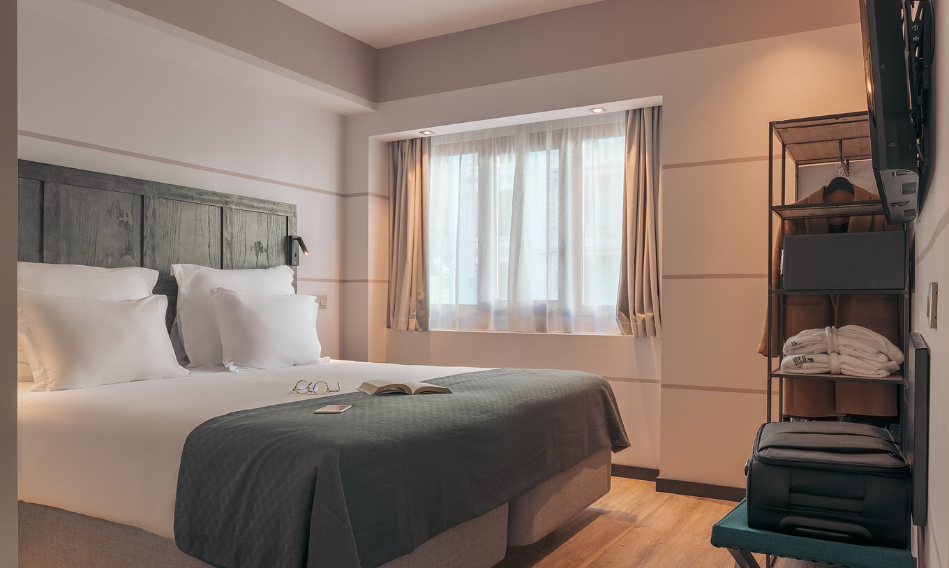 Le Double Deluxe Studio du Pestana Lisboa Vintage a un lit double avec une couverture grise et une armoire avec un manteau