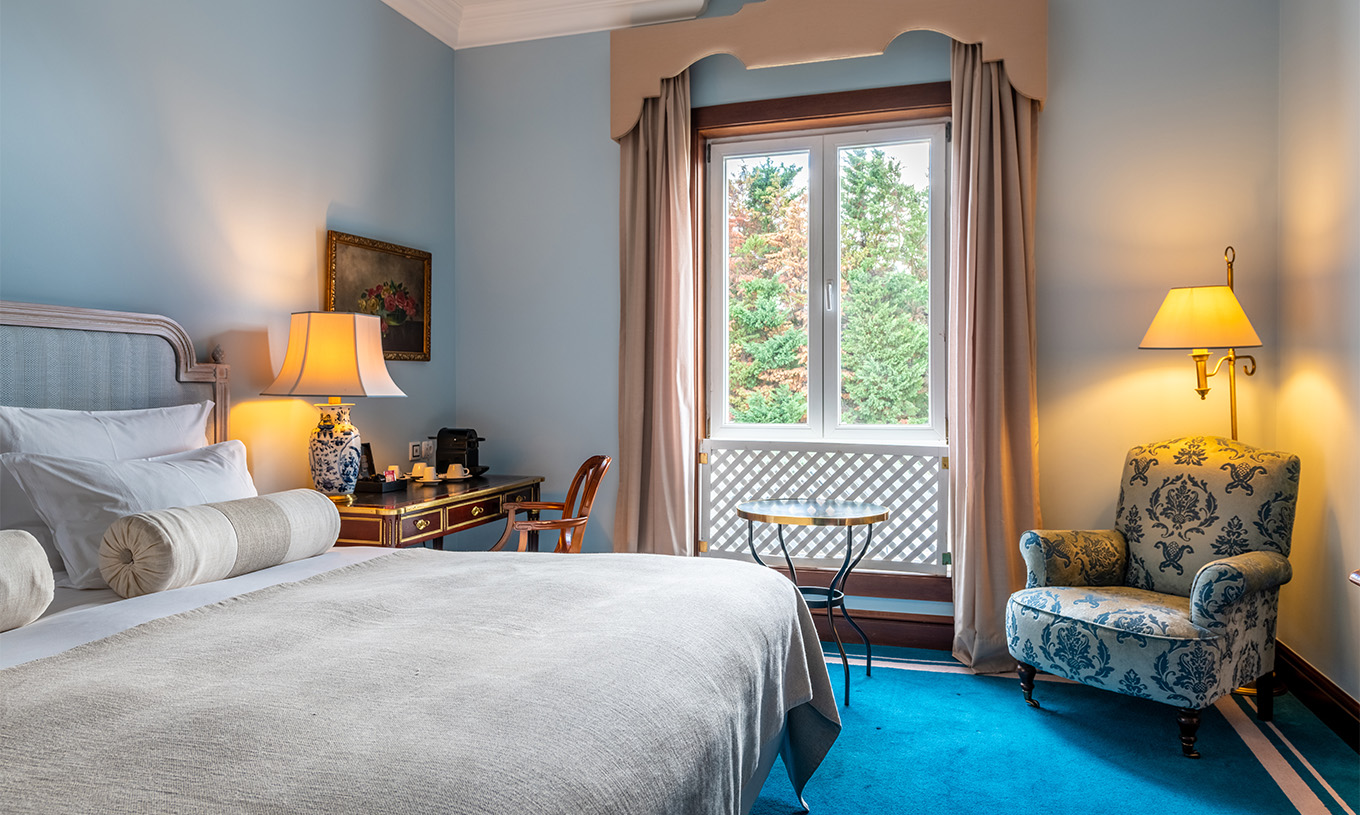 Le Deluxe du Pestana Palace Lisbonne a un lit double, un bureau, une fenêtre avec une grille décorative et moquette bleue
