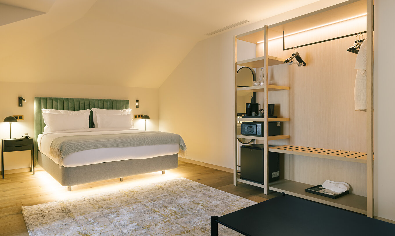 La Junior Suite du Pestana Rua Augusta Lisboa a un lit double illuminé et une armoire ouverte avec croisillons et étagères
