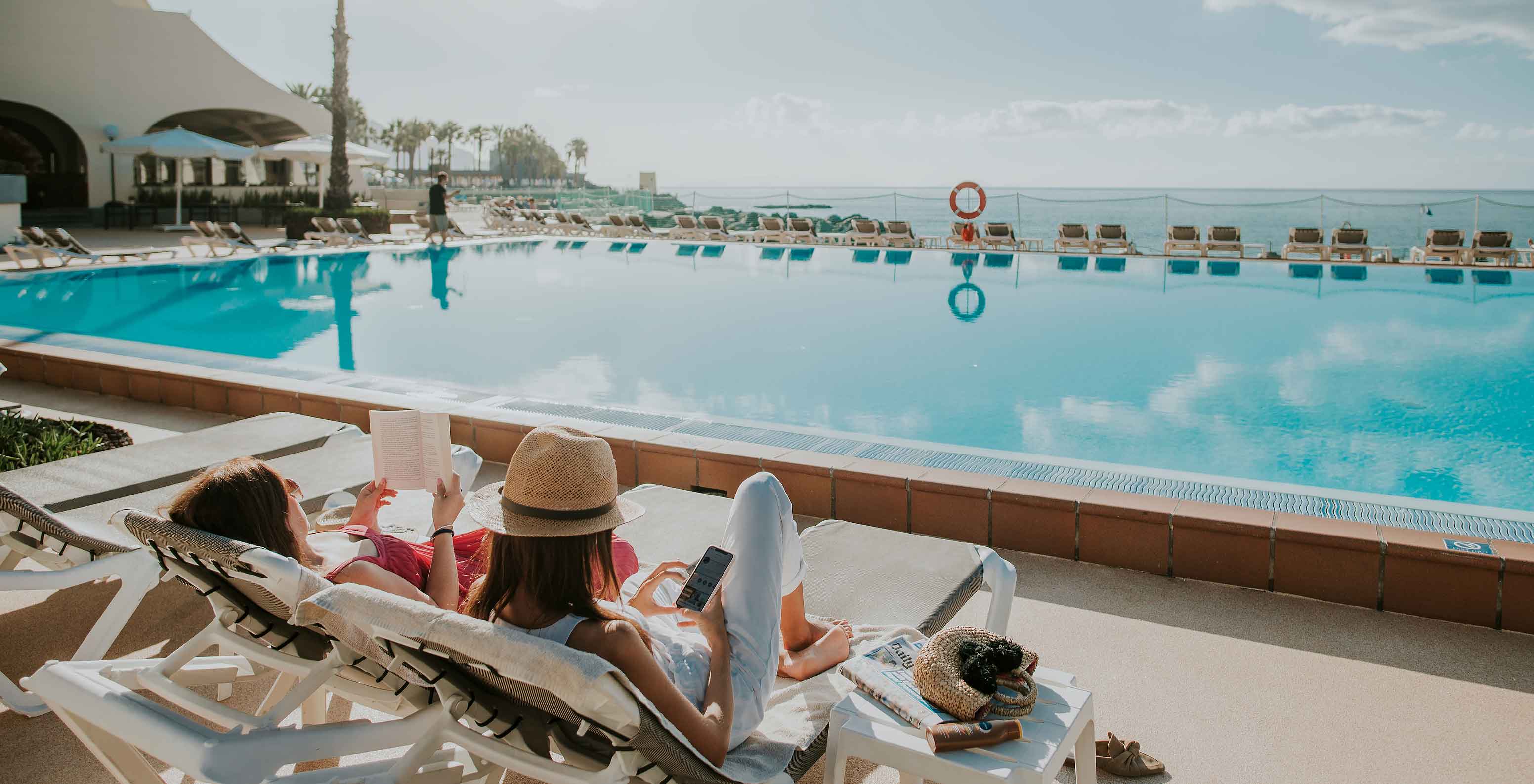 Deux dames sur des chaises longues au bord de la piscine du Pestana Madeira Beach Club, un complexe hôtelier de luxe