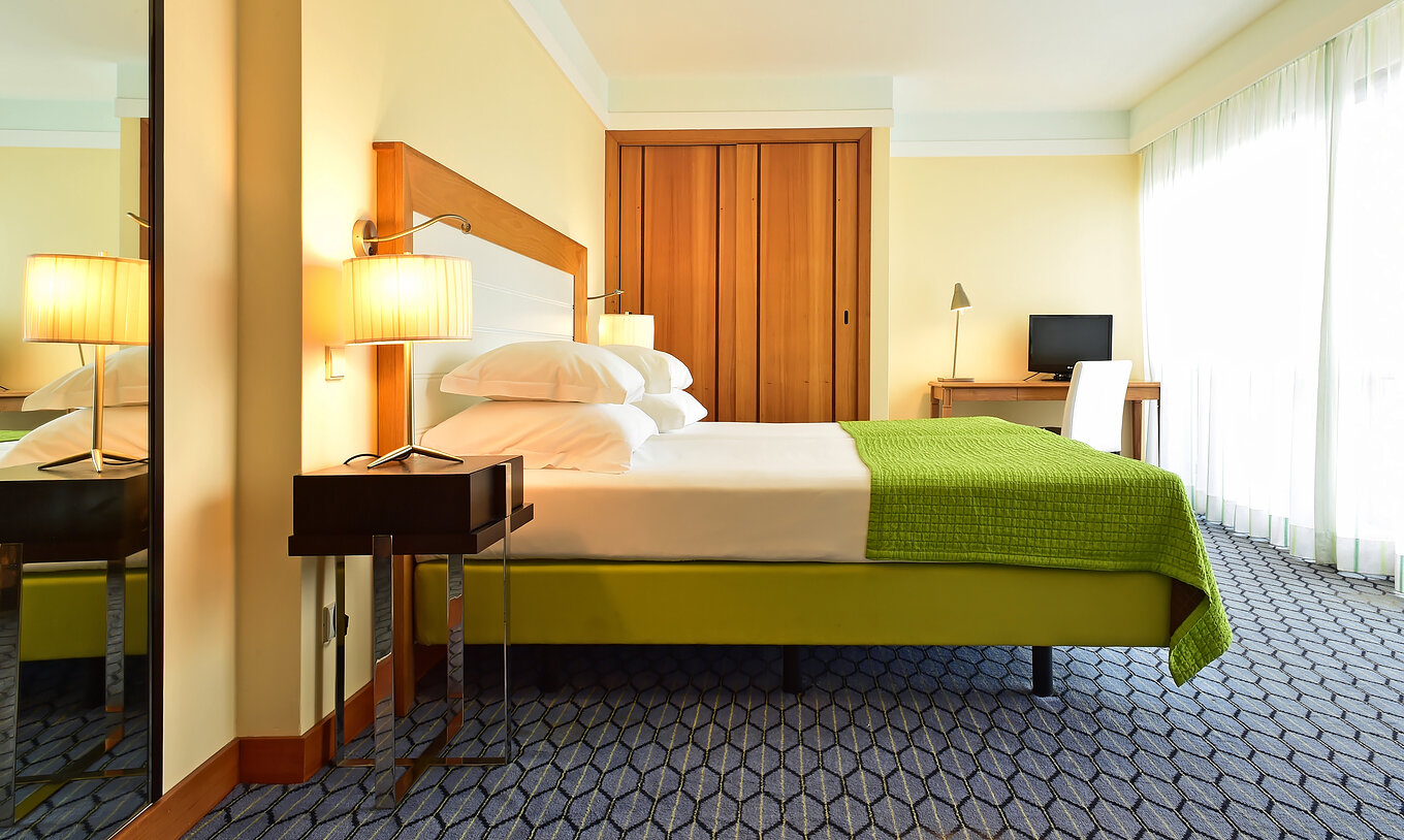 La Junior Suite du Pestana Promenade a un lit double avec une couverture verte, une armoire et un bureau