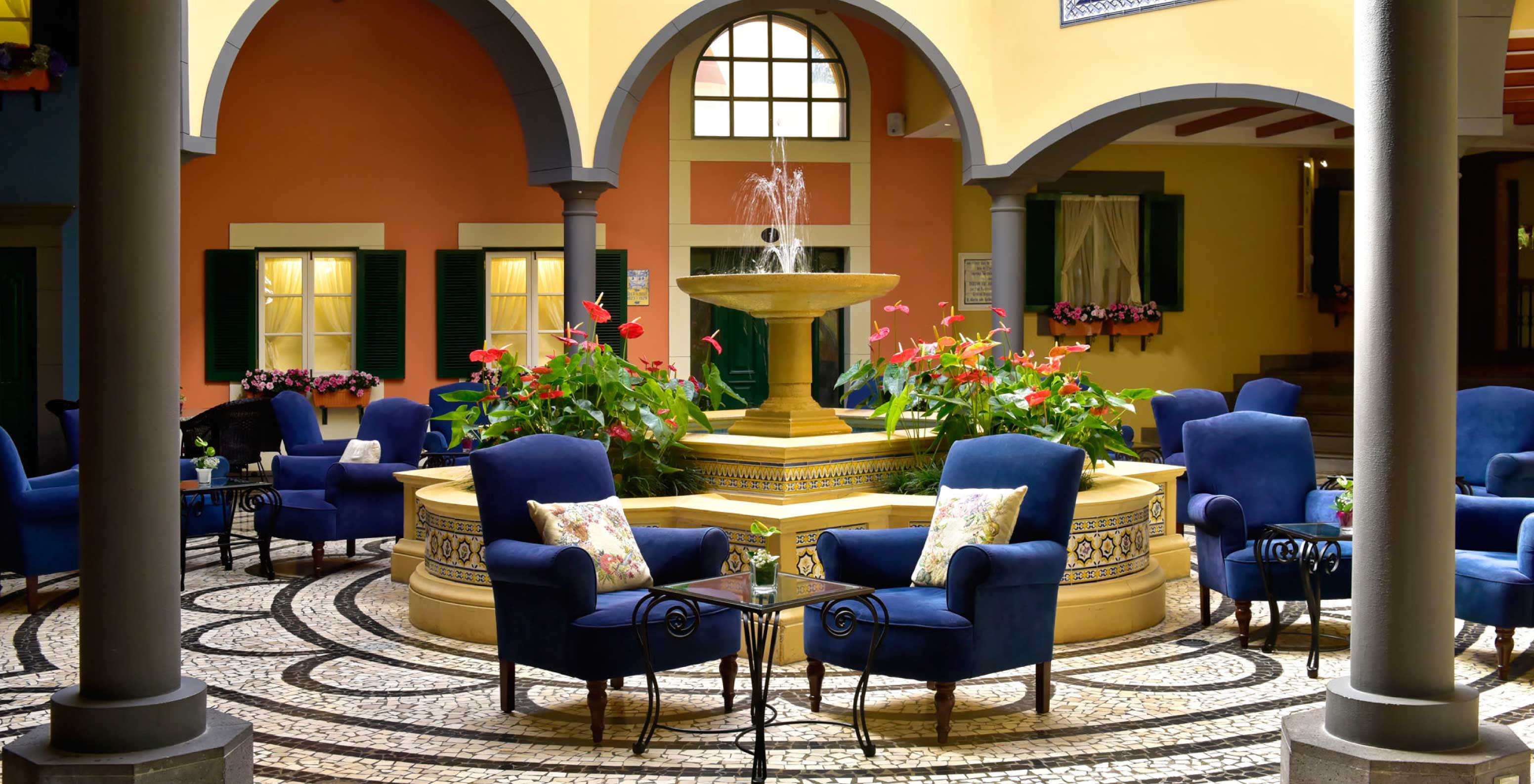 Le bar A Fonte, de l'Hôtel de Charme à Madère a une fontaine avec de l'eau et des fleurs et deux fauteuils bleus