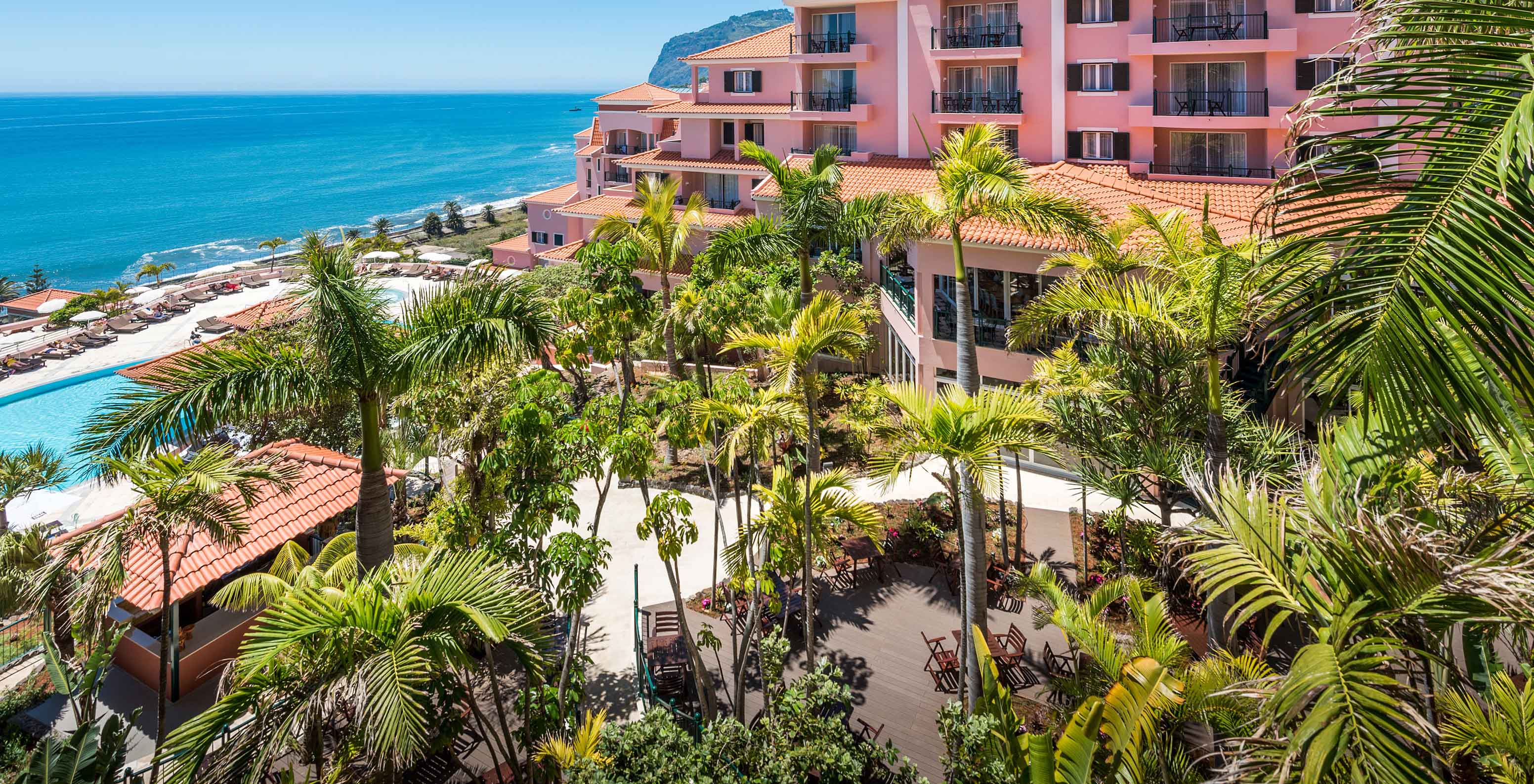Paysage du Pestana Royal All Inclusive, avec des bâtiments roses, de la végétation et l'océan en arrière-plan