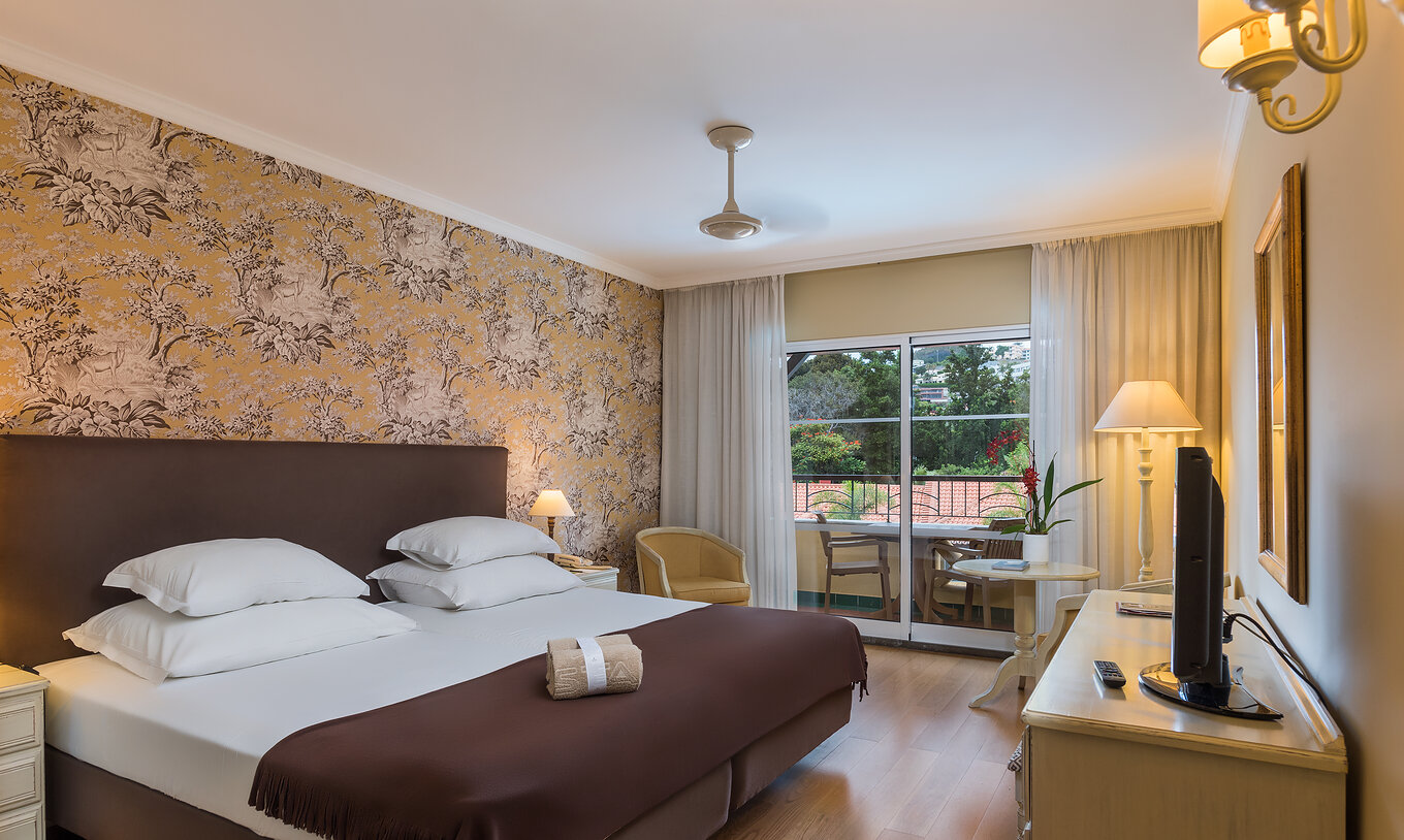 Le Studio Supérieur du Pestana Village a un lit double avec tête de lit et couvre-lit marron, papier peint floral et balcon