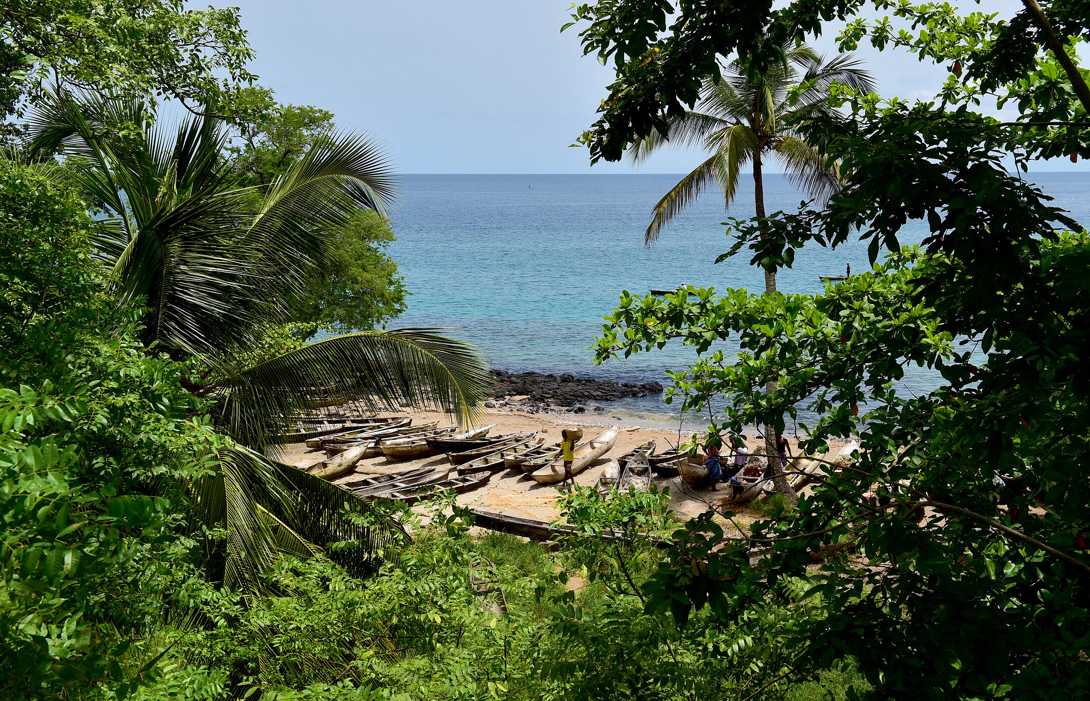 Vue d'une plage à São Tomé et Príncipe, entourée de végétation, avec des canoës sur le sable et la mer en arrière-plan.