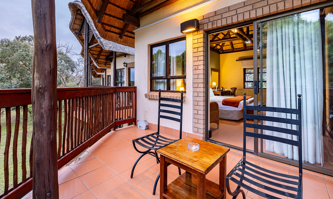 La Chambre Standard du Pestana Kruger Lodge a un balcon avec détails en bois deux chaises et une table d'appoint