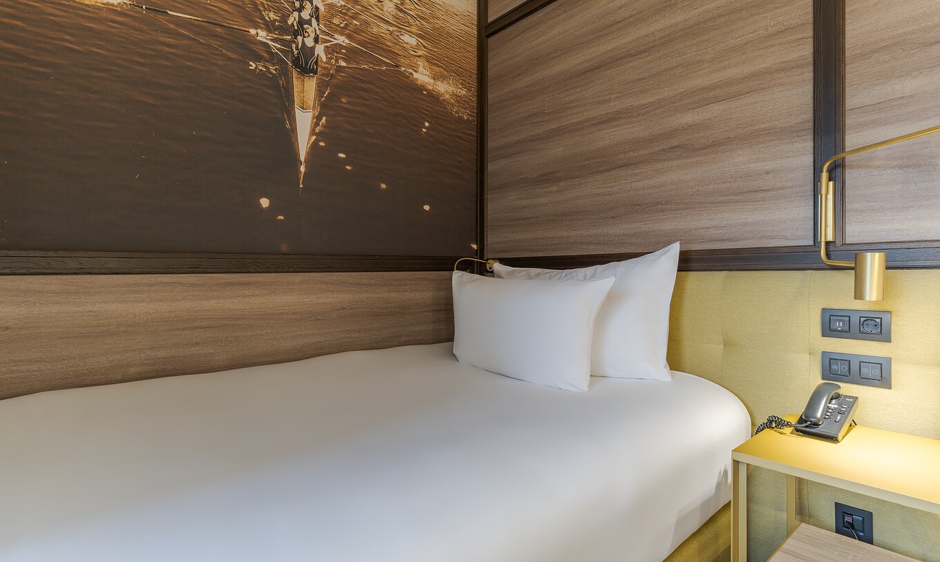 Chambre Cozy du Pestana CR7 Gran Vía Madrid avec lit blanc, tête de lit en bois et lampe dorée murale
