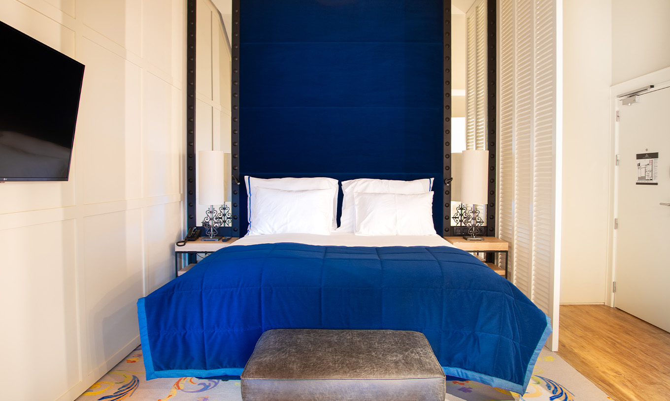 Le Loft du Pestana Plaza Mayor Madrid a un lit double avec une tête de lit bleue et des miroirs, et une télévision au mur