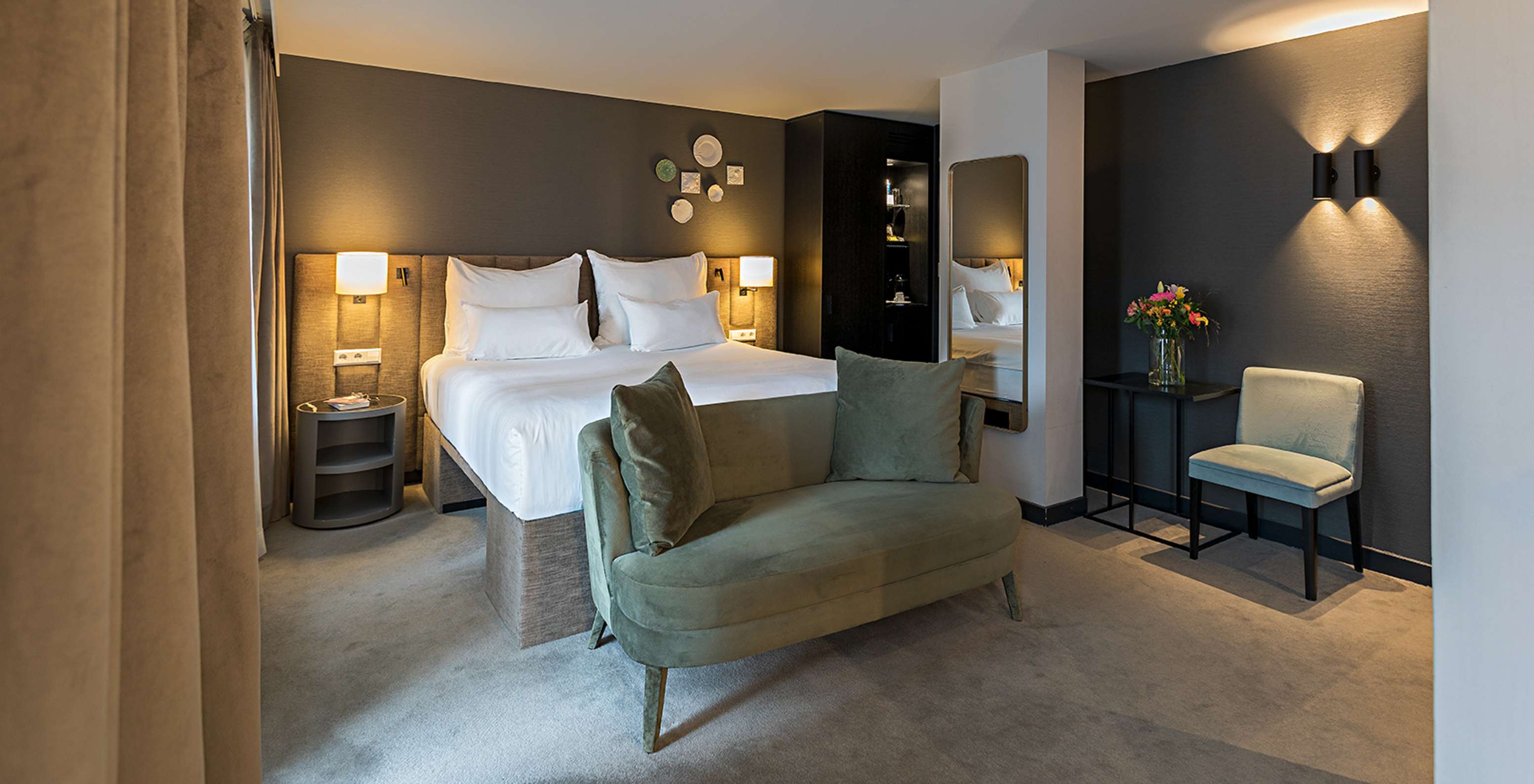 Chambre élégante avec grand lit blanc, banquette verte, éclairage tamisé et miroir mural moderne