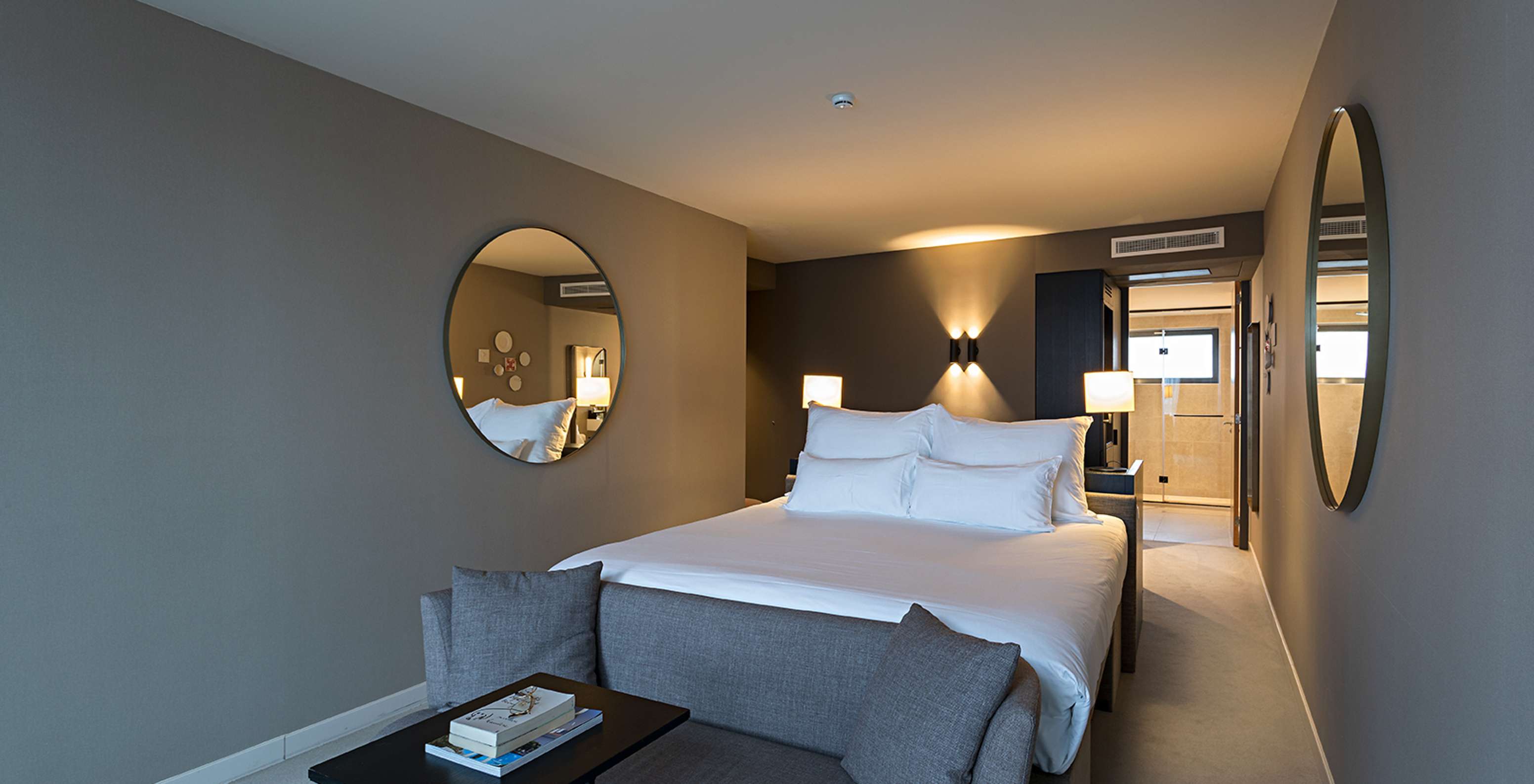 Chambre contemporaine avec grand lit blanc, miroirs ronds, éclairage tamisé et salle de bain au fond