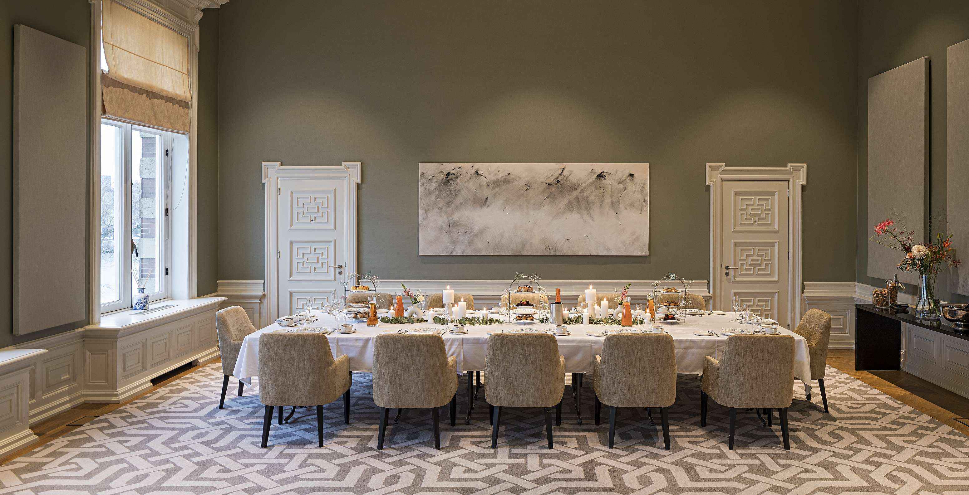 Grande salle de réception avec longue table dressée, bougies, fauteuils beiges et tableau mural moderne