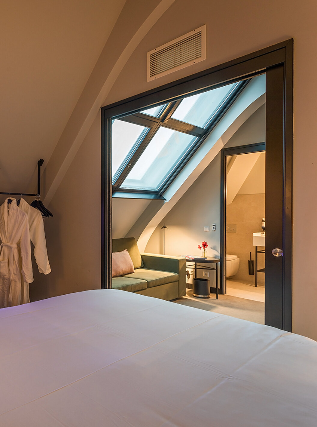 La chambre Loft du Pestana Amsterdam Riverside a un canapé vert, avec une table basse, et deux peignoirs