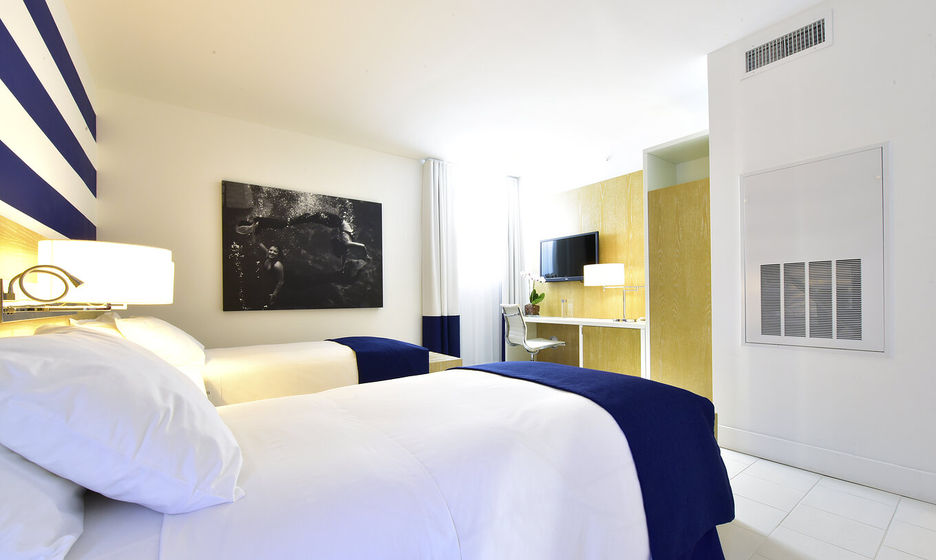 La chambre Art Deco Double du Pestana Miami South Beach a deux lits simples, télévision, table et un grand tableau