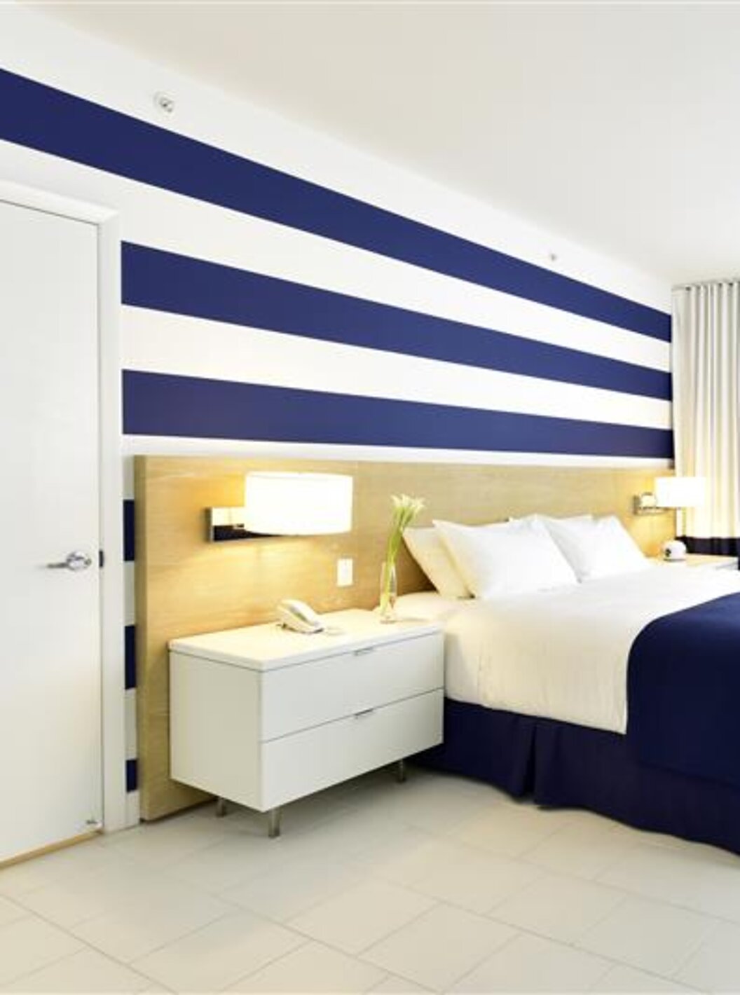 Chambre moderne avec lit double, déco bleu-blanc et lumière naturelle.