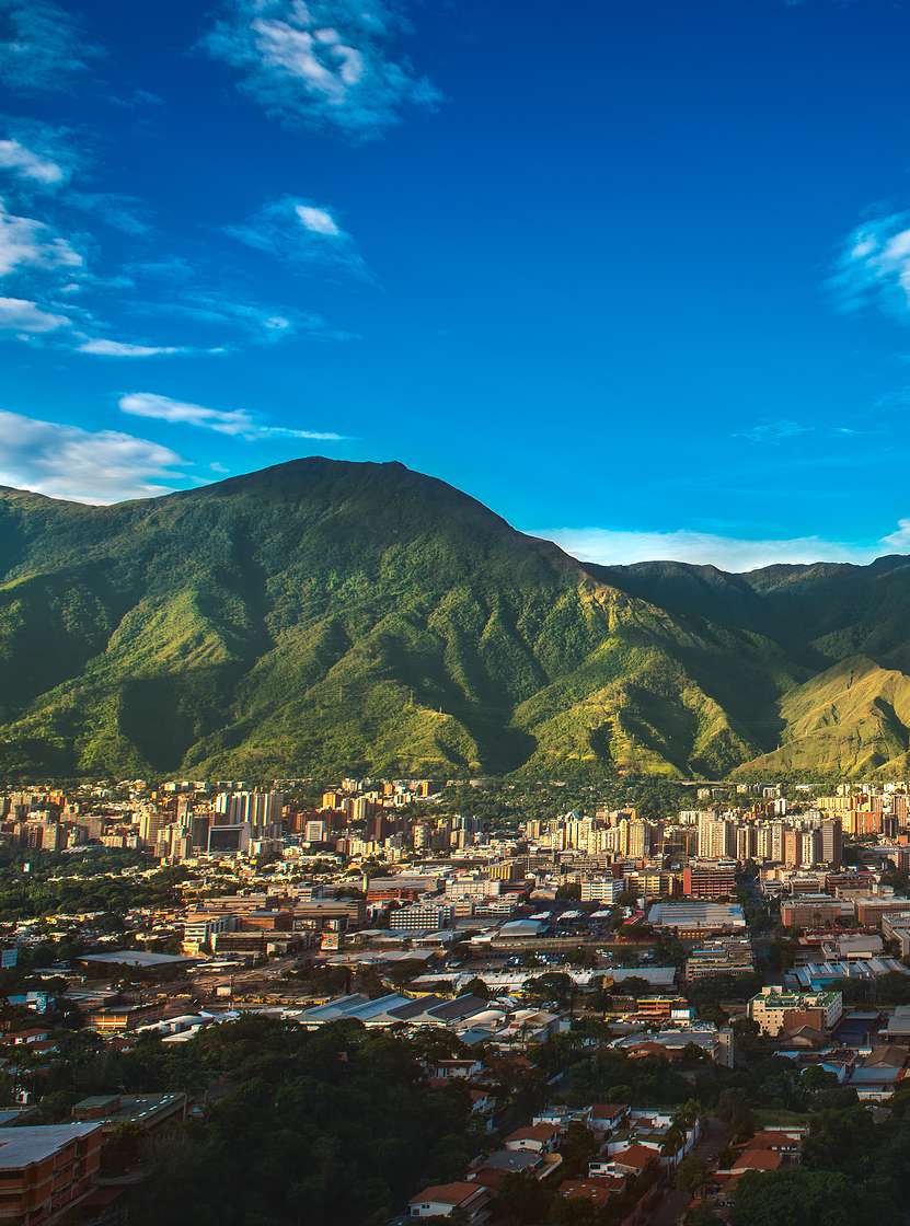 Vue aérienne de la ville de Caracas, avec de hauts bâtiments, contrastant avec la nature montagneuse et le ciel bleu