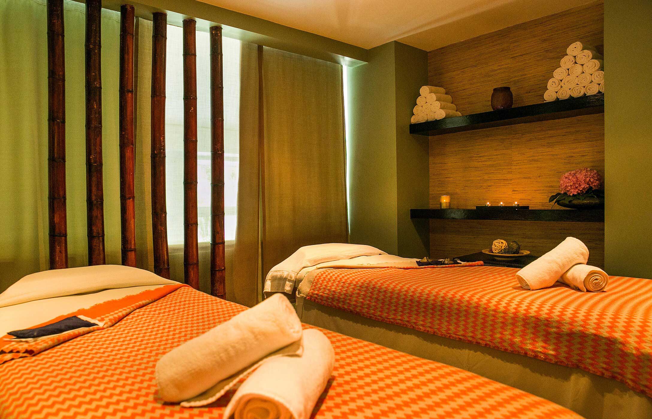 Salle de spa relaxante avec deux tables de massage couvertes de plaids orange, entourées de bambou, au Pestana Palace Spa