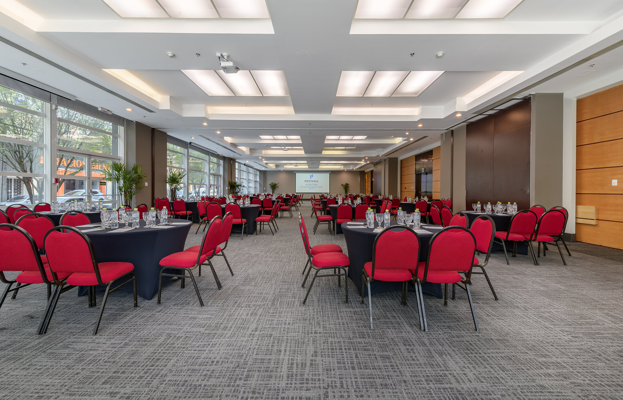 Salle de réunion ou de conférence, avec plusieurs tables rondes, des chaises rouges, des verres et des bouteilles d'eau
