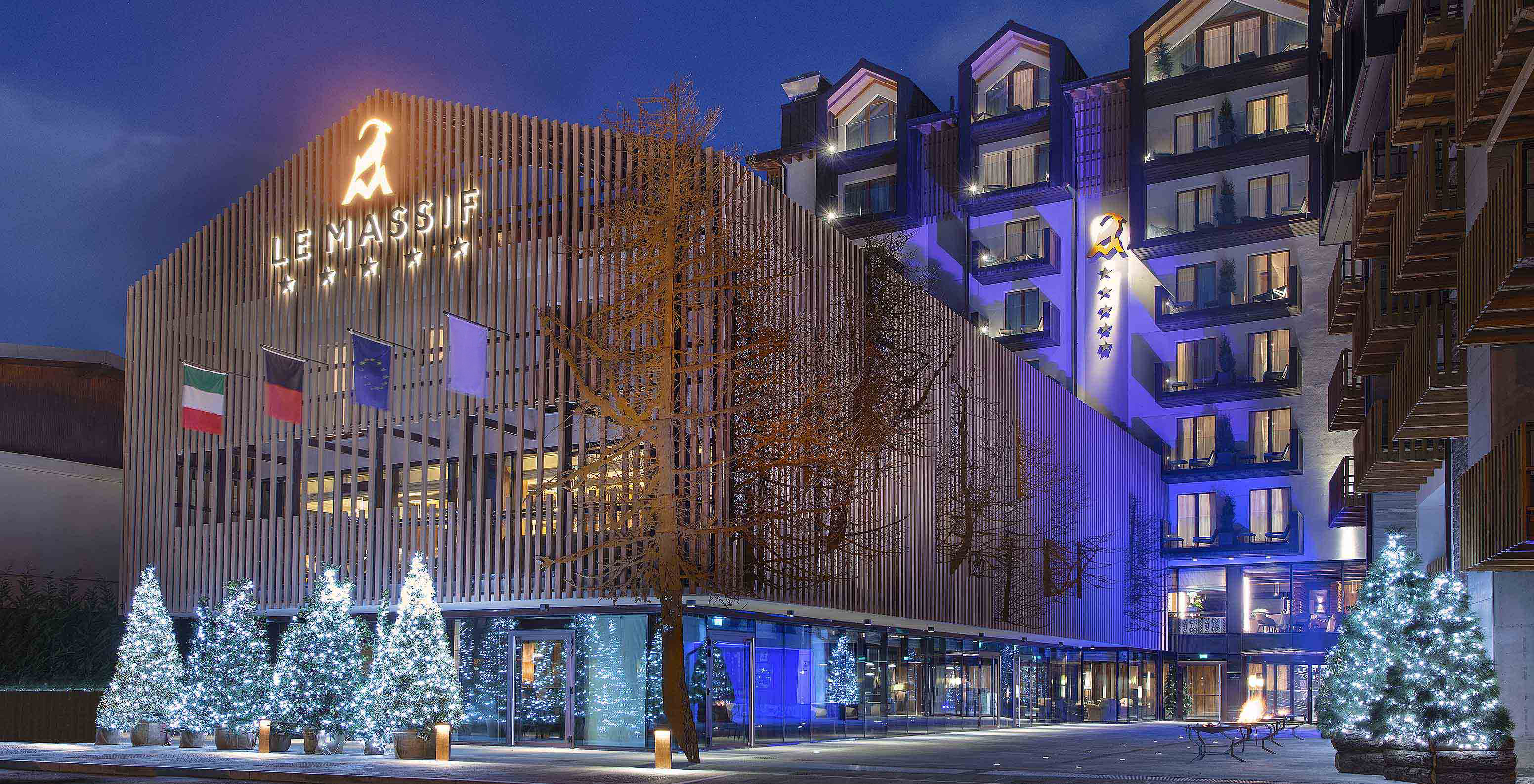 Fachada do Le Massif Courmayeur, Hotel nos Alpes Italianos em Courmayeur para fazer ski, iluminada à noite com árvores decoradas
