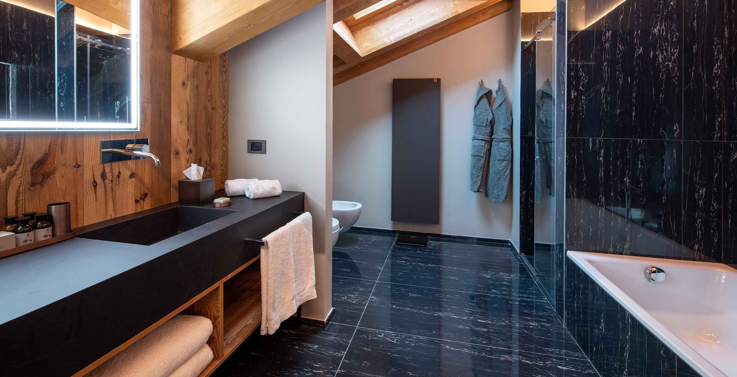 Casa de banho moderna no Le Massif Courmayeur, Hotel nos Alpes Italianos em Courmayeur para fazer ski, com lavatório em pedra escura, banheira branca e paredes em madeira e mármore