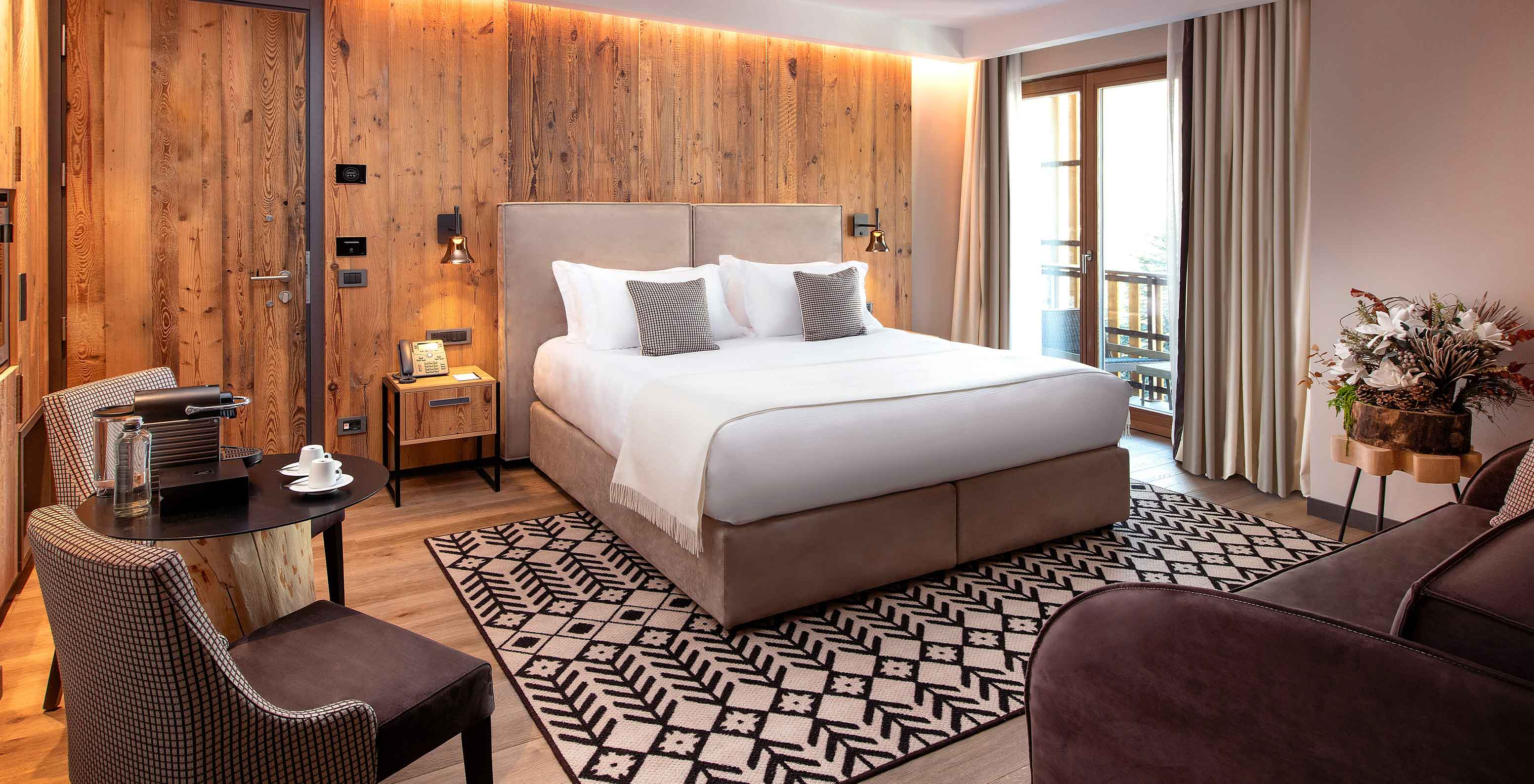 Quarto Le Massif View do hotel Le Massif Courmayeur com cama de casal, mesa de café e varanda com cortinas