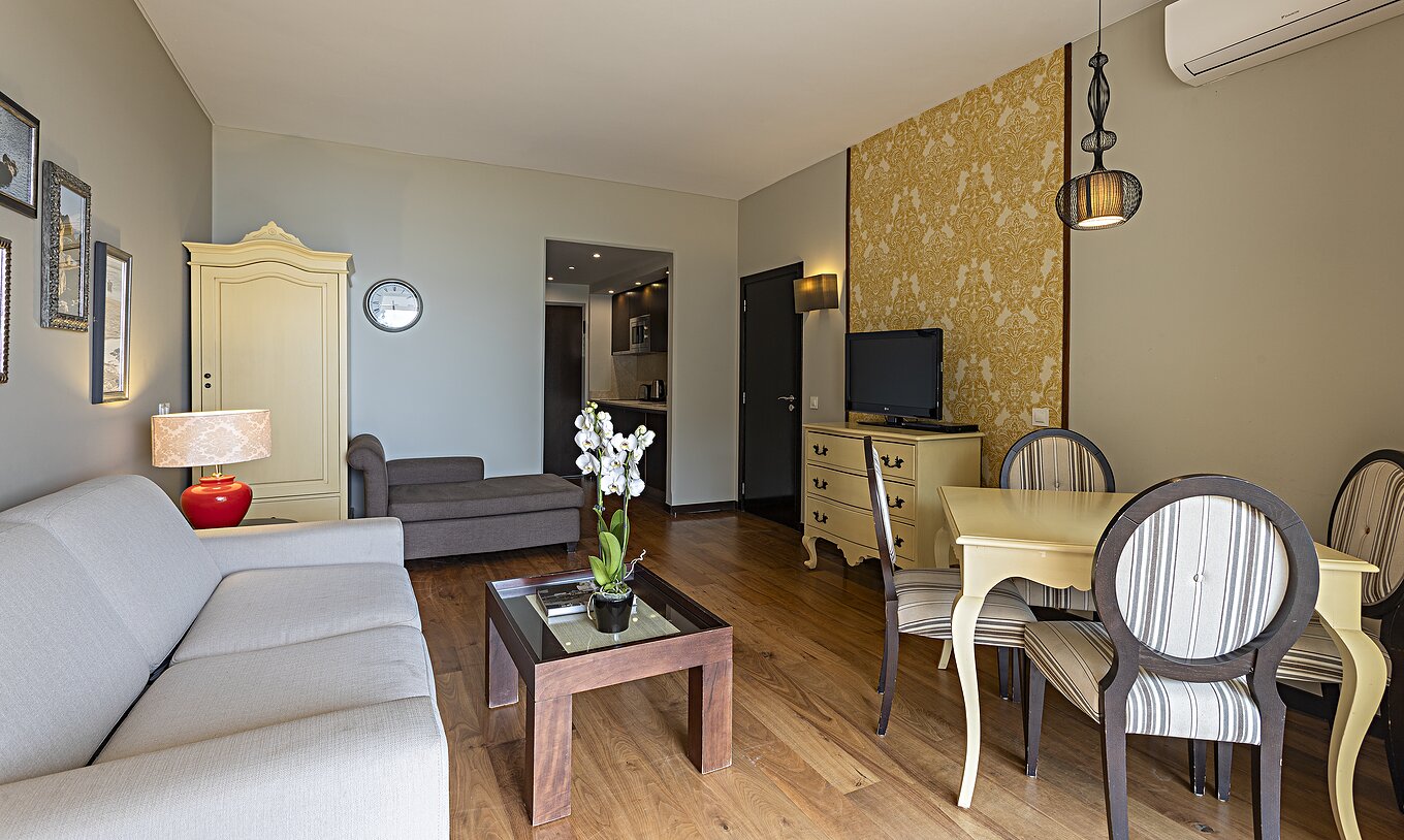 De Cliff Suite T1 bij Pestana Alvor Praia heeft een woonkamer met een bank, behang, televisie en een eettafel