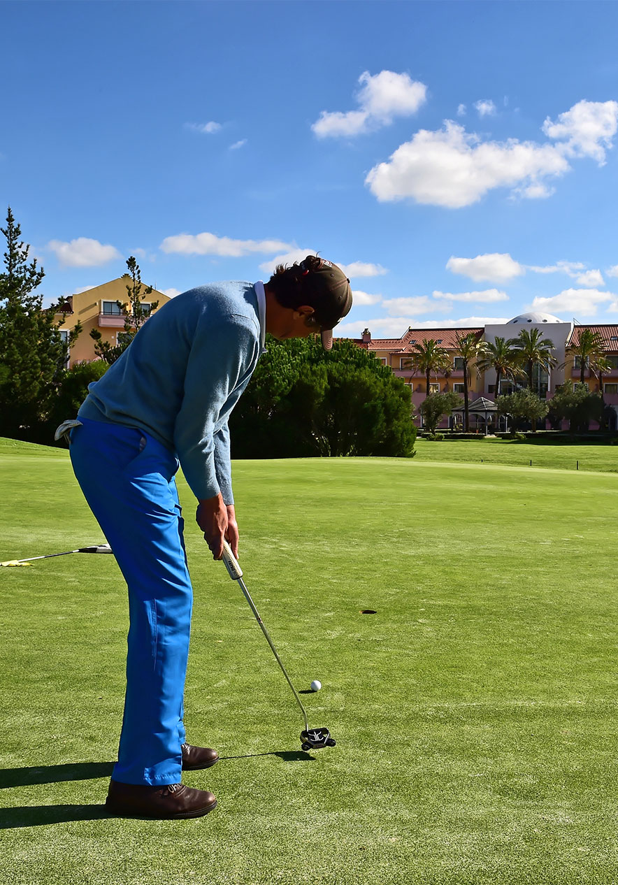 Golfer die een putt slaat op een zonnige golfbaan met palmbomen en gebouwen onder een blauwe lucht