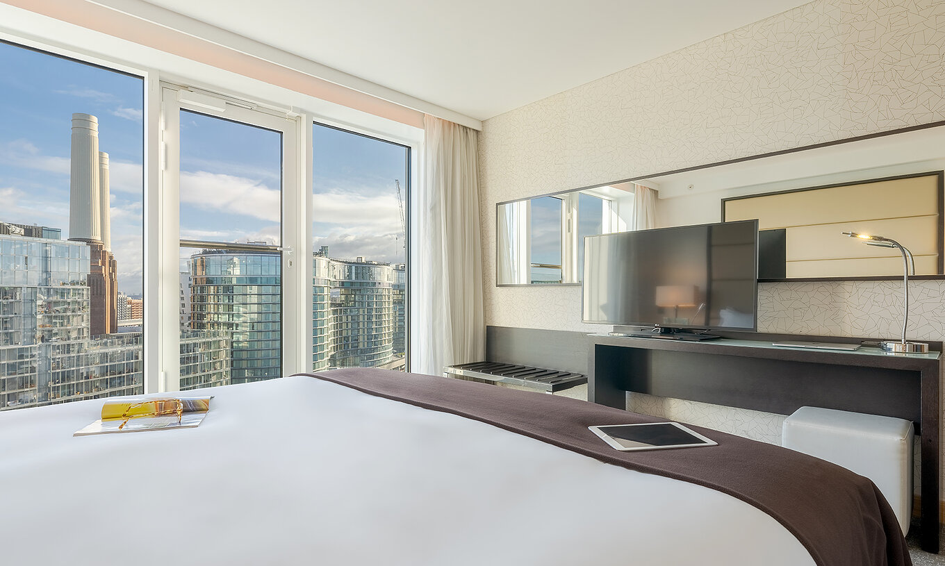 De Superior King van Pestana Chelsea Bridge heeft bed, bureau met tv, bank en ramen met uitzicht op de stad