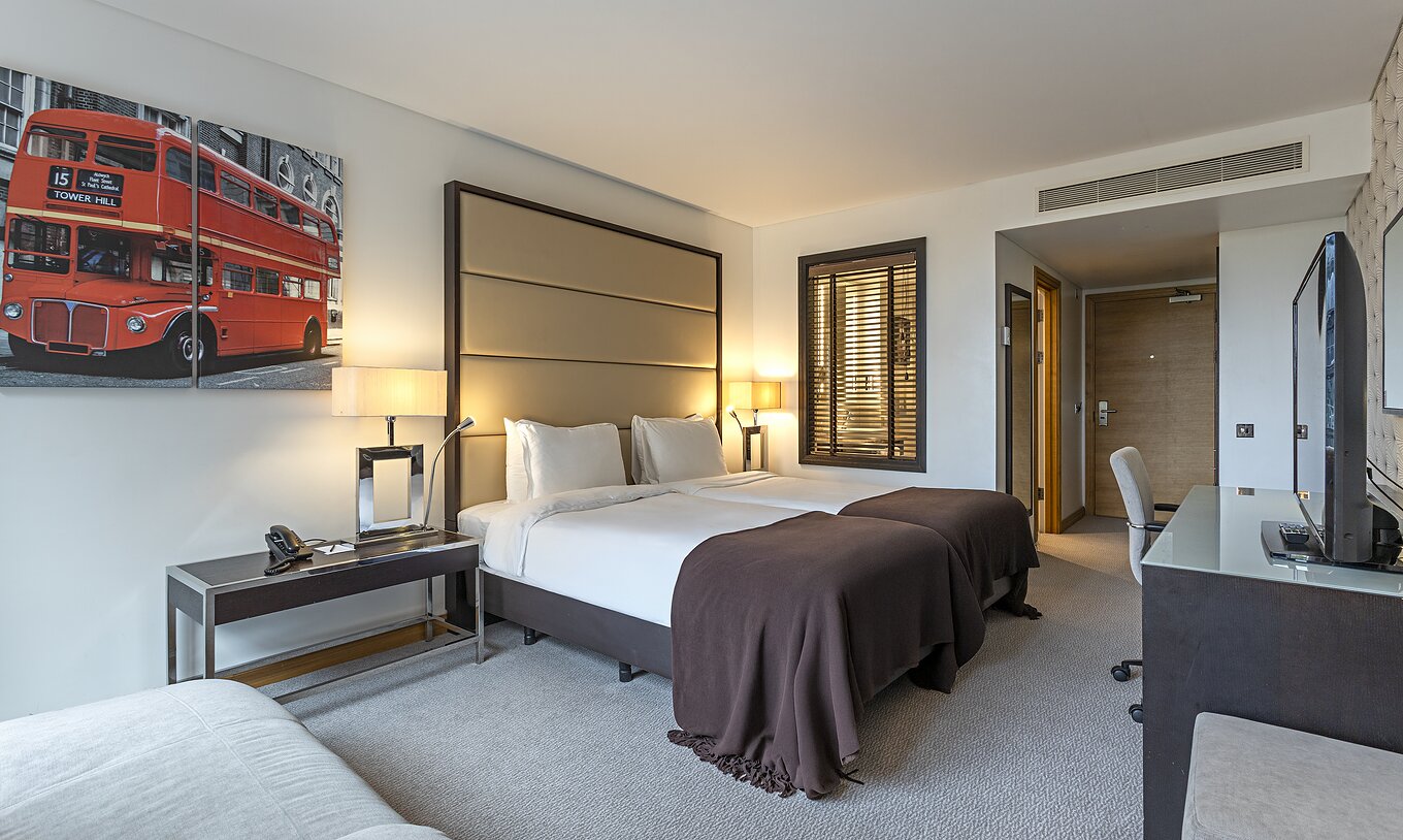 Grand Deluxe kamer van Pestana Chelsea Bridge met tweepersoonsbedden, bureau en foto van rode bus aan muur