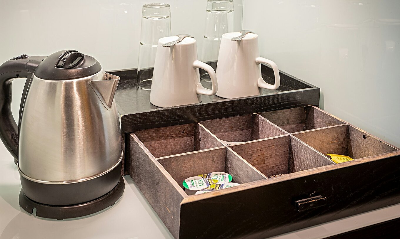 Grand Deluxe-kamer van Pestana Chelsea Bridge met waterkoker, kopjes en houten theelade op tafel met glazen