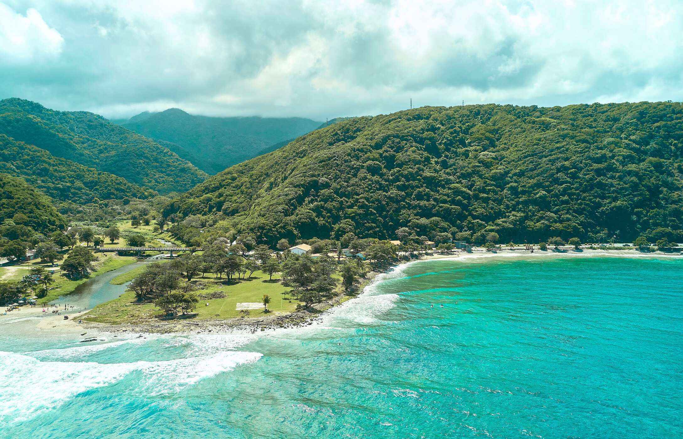 Luchtzicht op het strand van La Punta in Venezuela, met kristalhelder water, omgeven door groene bergen.