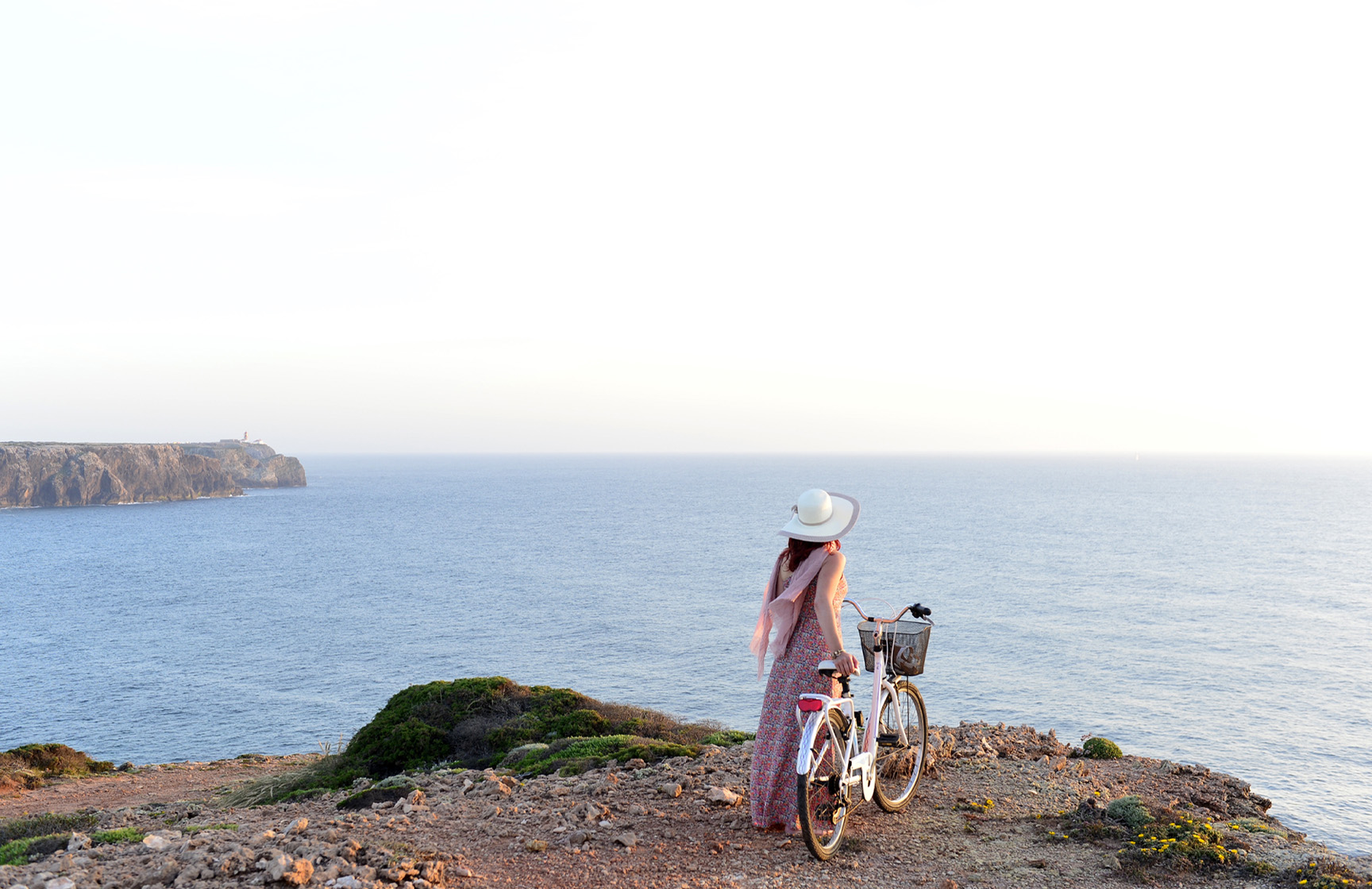 Vrouw loopt met een fiets in de hand langs de kliffen aan de Portugese kust, aangeboden door Pousadas de Portugal