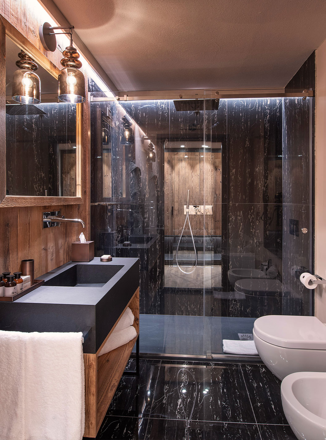Quarto Deluxe do Le Massif Courmayeur com banheiro em mármore escuro, box de vidro e bancada de madeira