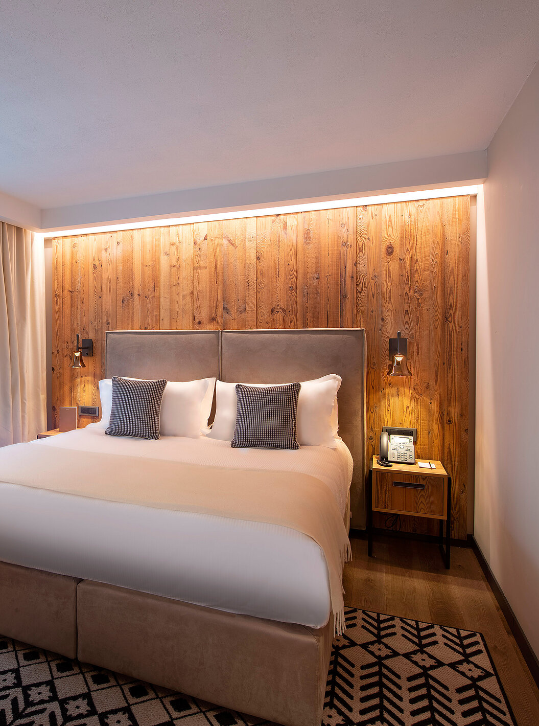 Quarto Deluxe no Le Massif Courmayeur com cama ampla, parede de madeira iluminada e janela com cortinas