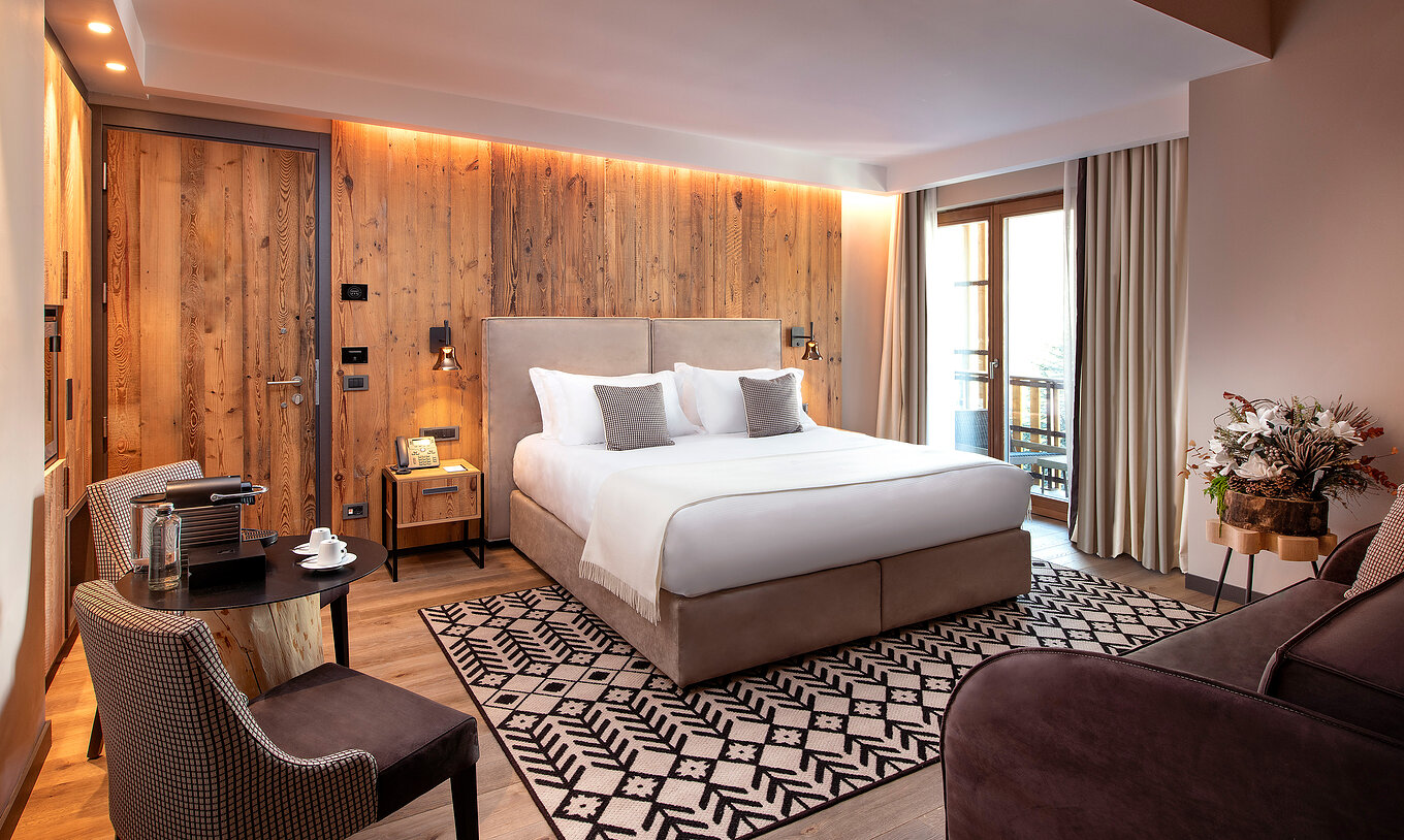 Suíte Familiar no Le Massif Courmayeur com cama ampla, painel de madeira, poltronas e varanda iluminada