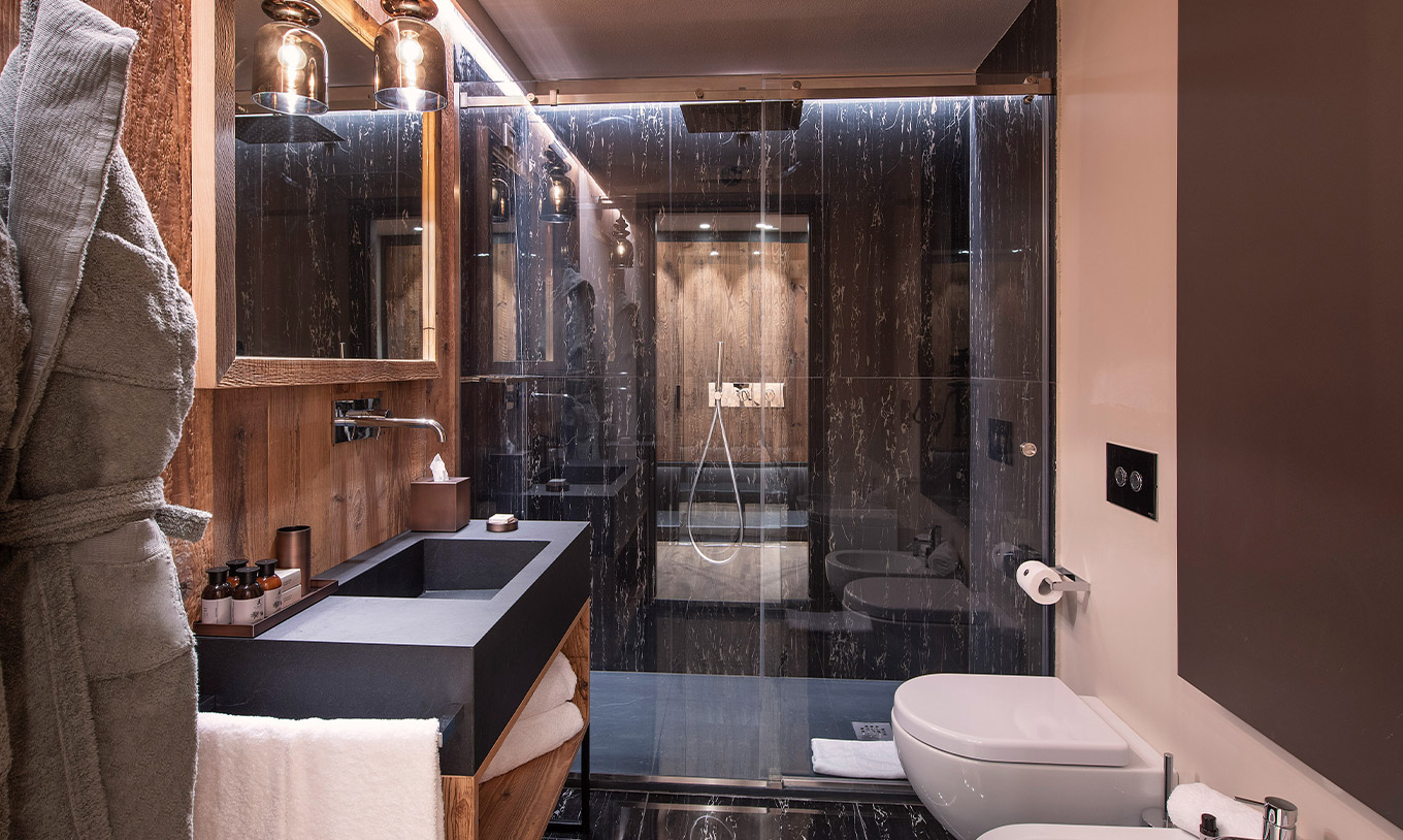 Quarto Grand Deluxe do Le Massif Courmayeur com banheiro em mármore escuro, bancada ampla e box de vidro