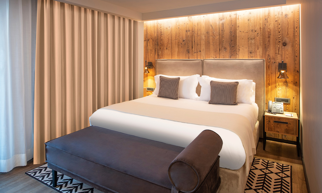 Quarto Grand Deluxe do Le Massif Courmayeur com cama ampla, painel de madeira e iluminação aconchegante