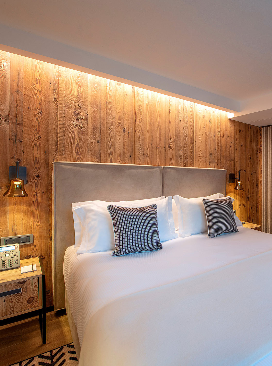 Suíte do Le Massif Courmayeur com cama ampla, paredes de madeira iluminadas e área de estar ao fundo