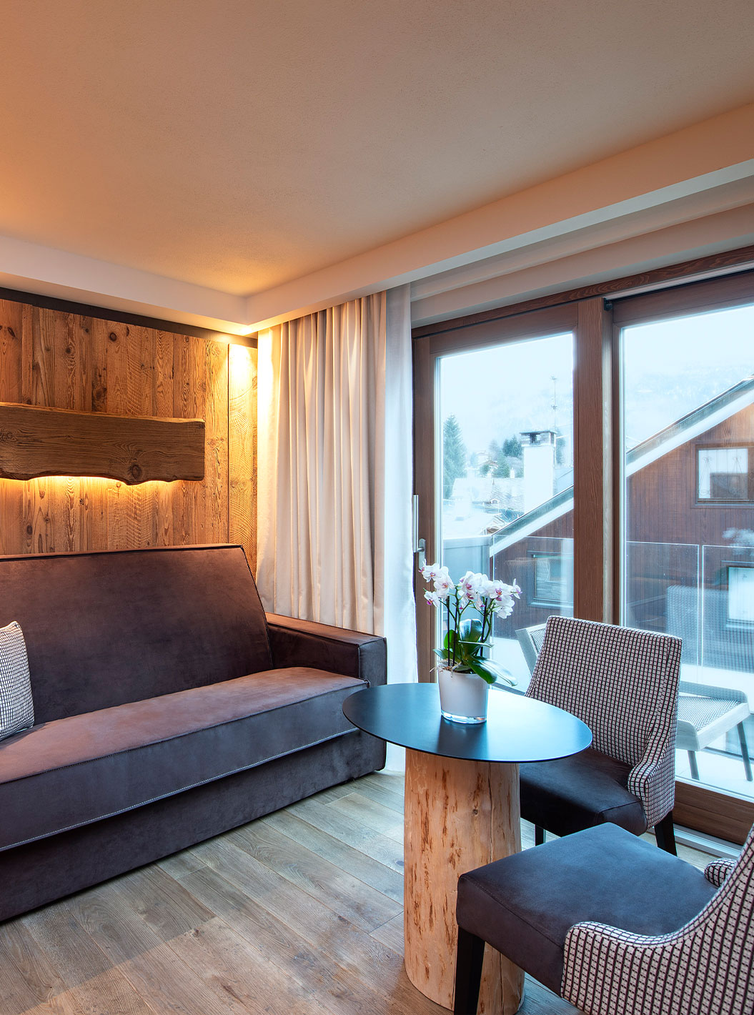 Suíte Le Massif Courmayeur com sala aconchegante, mesa redonda e vista para casas nevadas pela janela