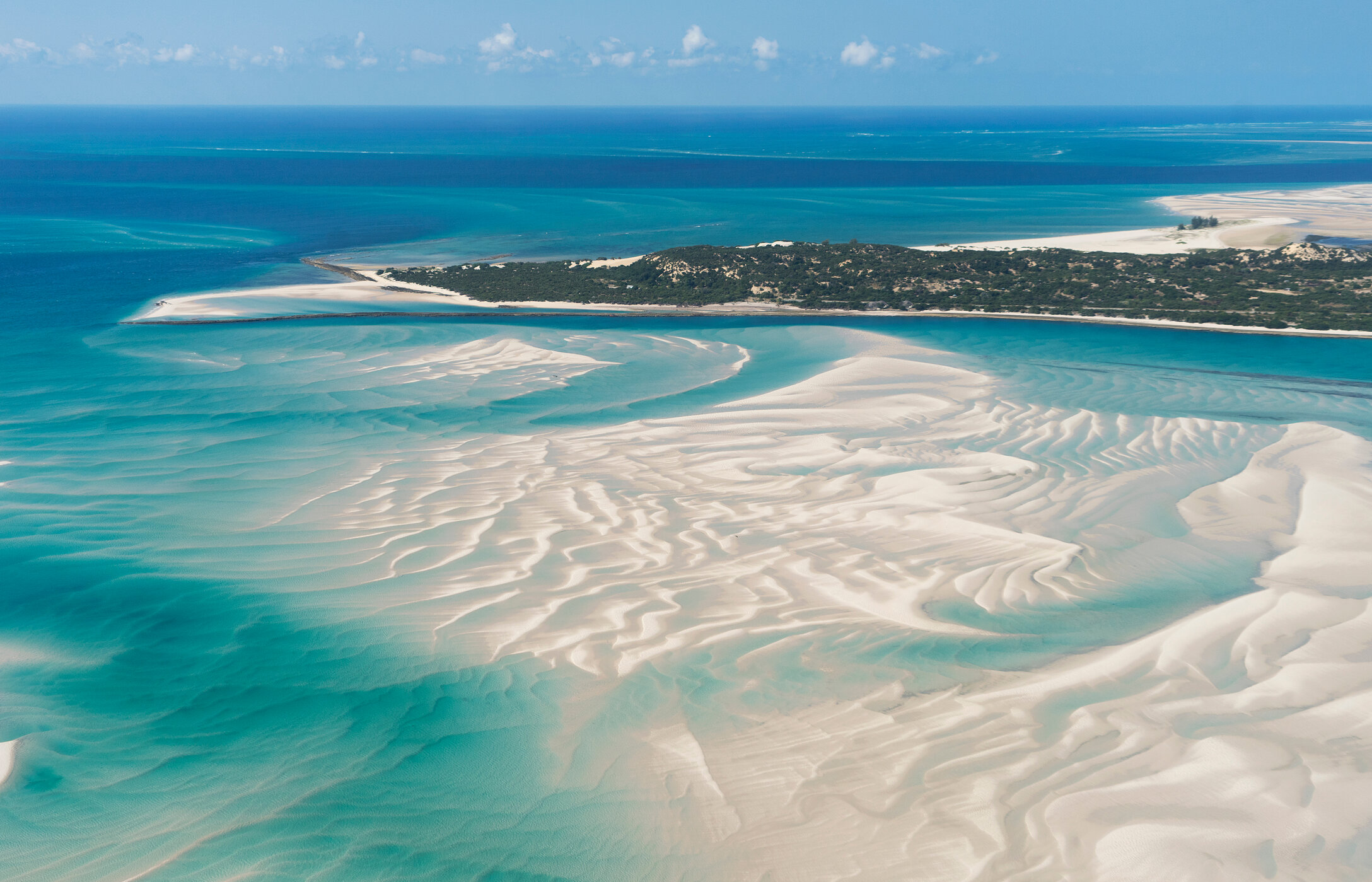Vista aérea da ilha Vilankulo, em Moçambique, com águas cristalinas, vários bancos de areia no mar, e vegetação ao fundo