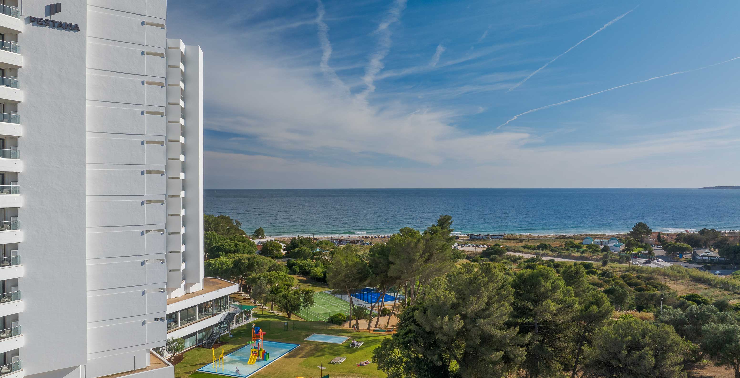 Vista exterior do hotel Pestana Blue Alvor Beach, onde se vê a vegetação verde e o mar azul ao fundo