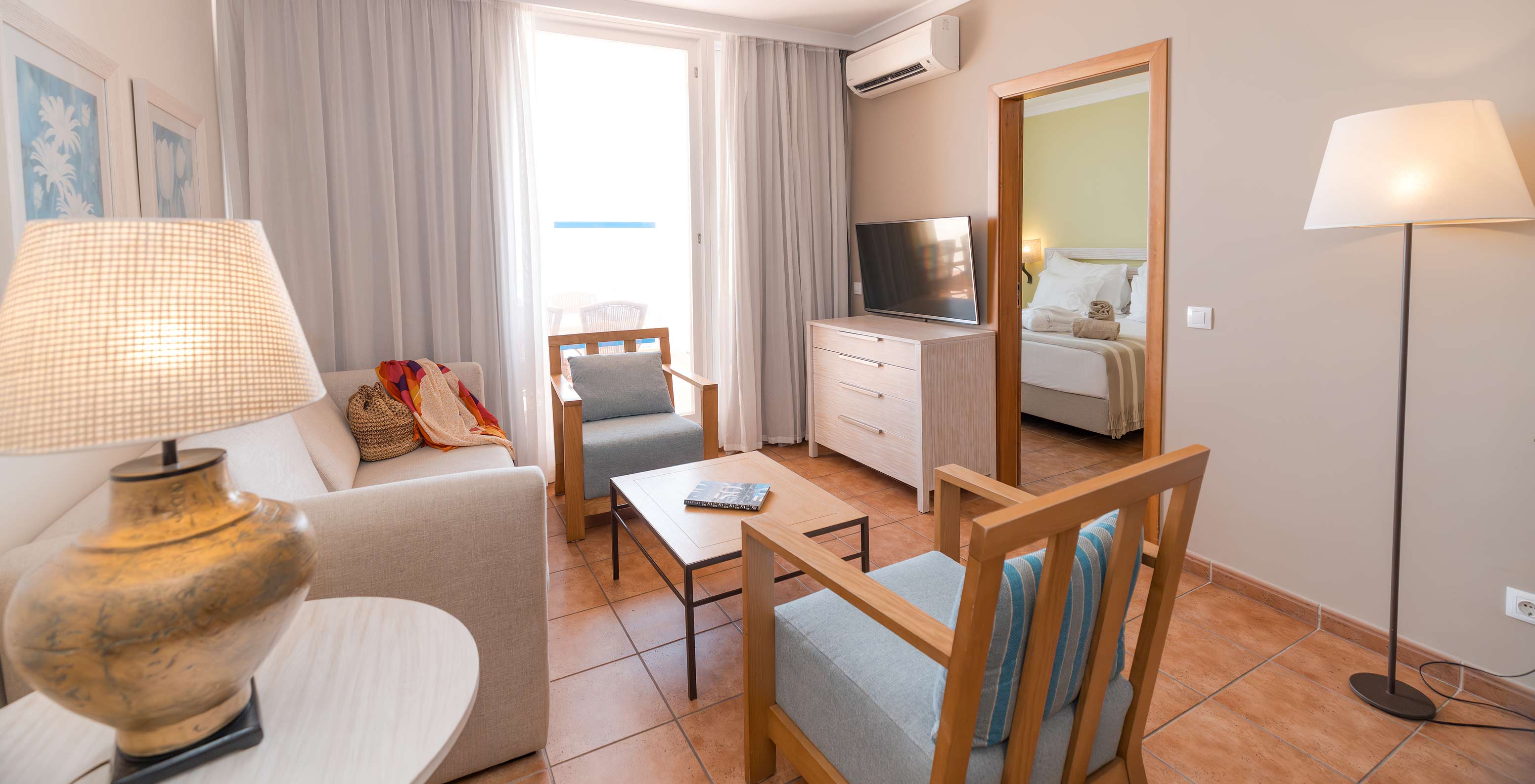 A Suite Superior Vista Mar do Pestana Viking tem uma sala com sofá, poltronas, televisão, ar condicionado e acesso à varanda