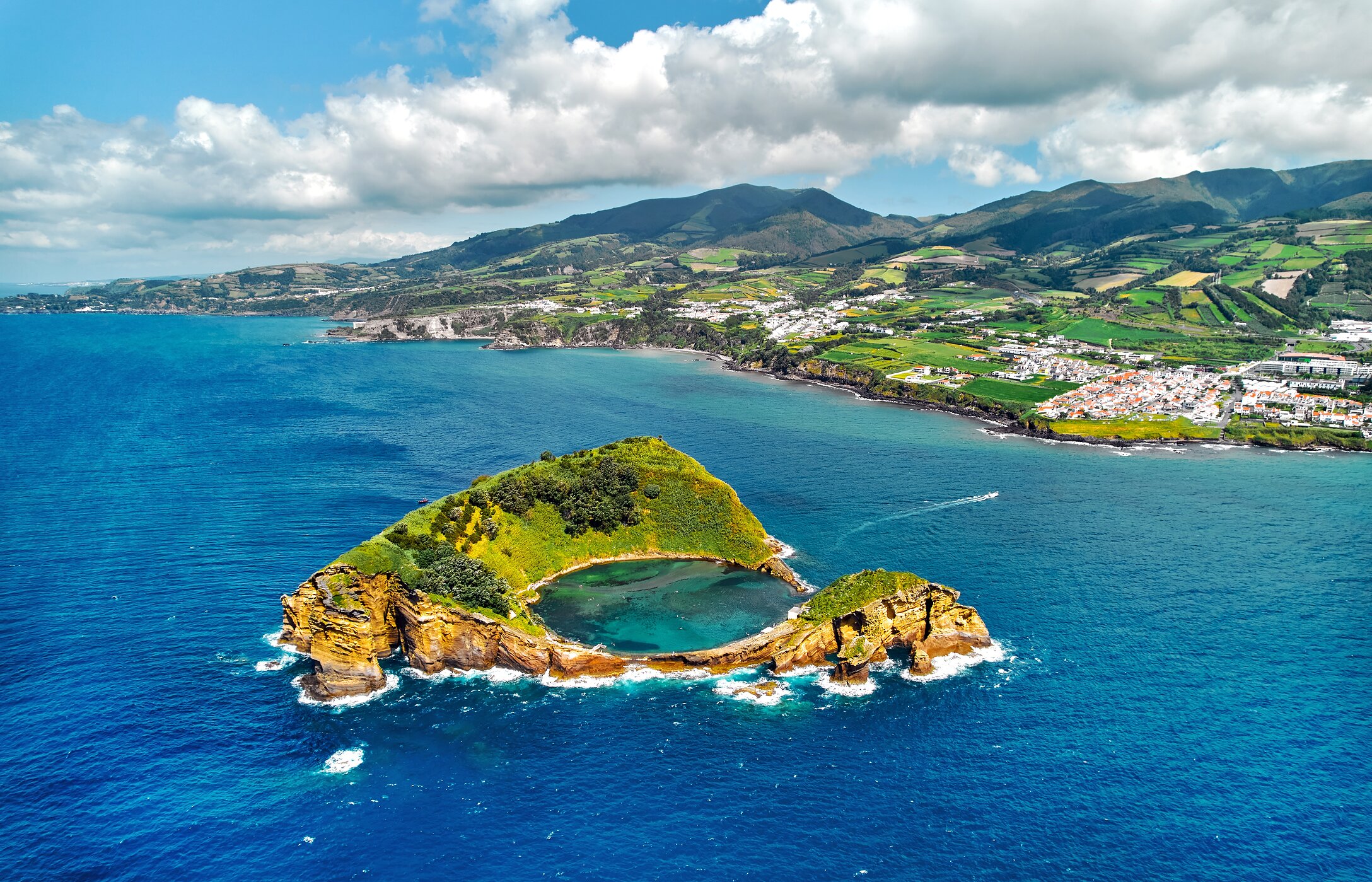 Vista panorâmica de Vila Franca do Campo, com uma ilhota em forma de anel no oceano, e colinas verdes ao fundo