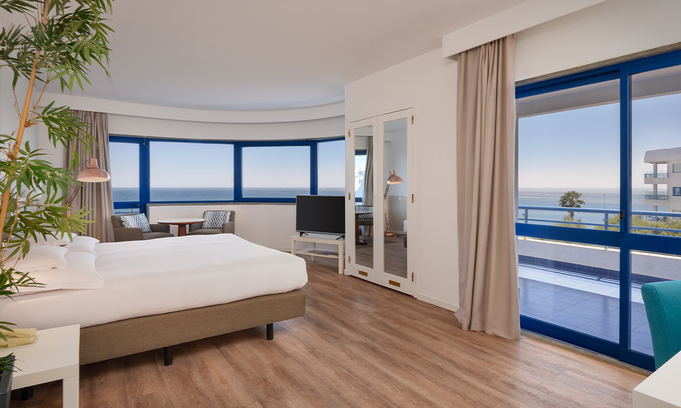 O quarto Deluxe Superior Vista Mar do Pestana Cascais conta com cama de casal, televisão, espelho e vista panorâmica para o mar 