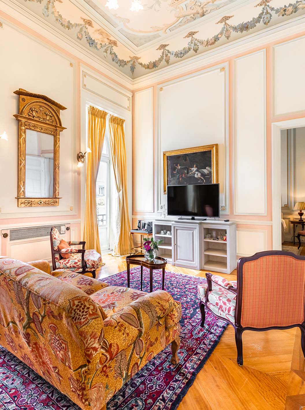 A Suite D. Amélia do Pestana Palace Lisboa tem uma sala de estar com sofá, cadeiras, televisão e duas janelas grandes